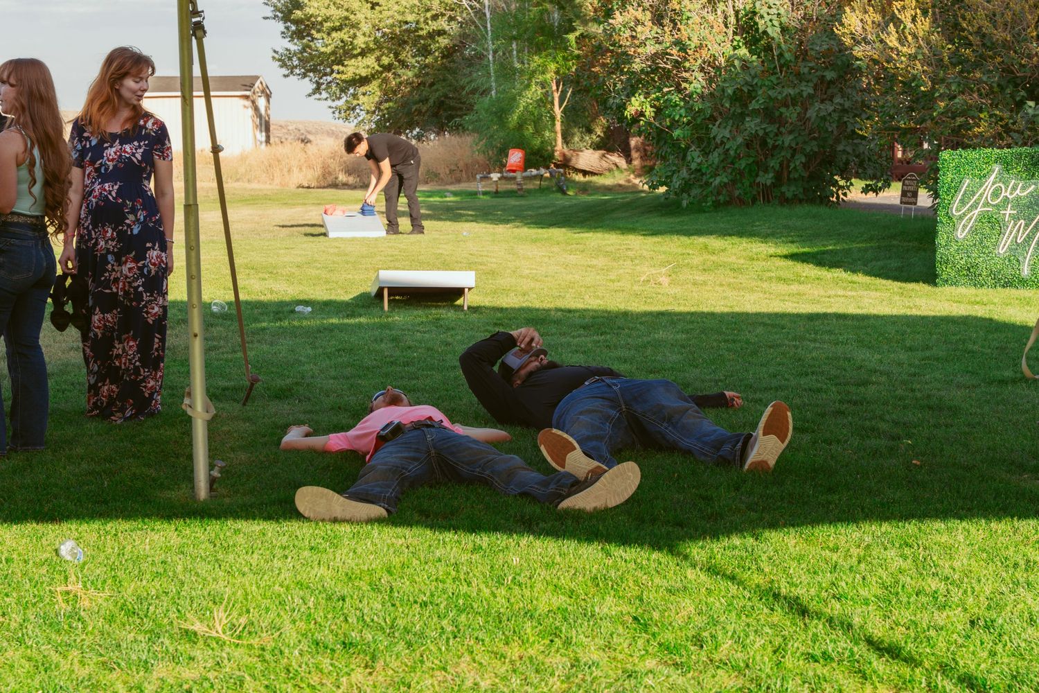People lying down and relaxing on a grassy lawn under trees.