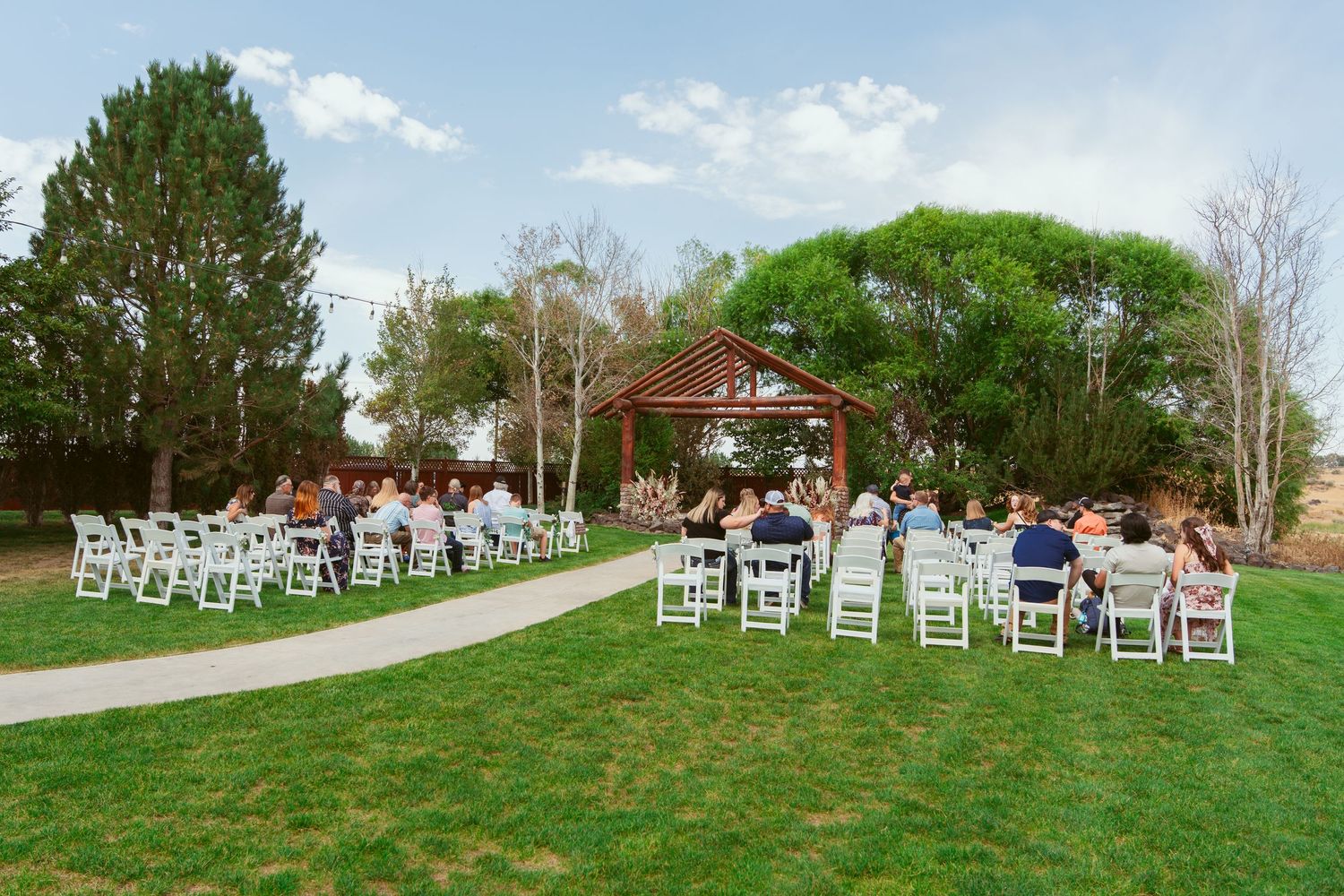 White wedding chairs set up on a grassy hillside for an outdoor ceremony with trees in the background.