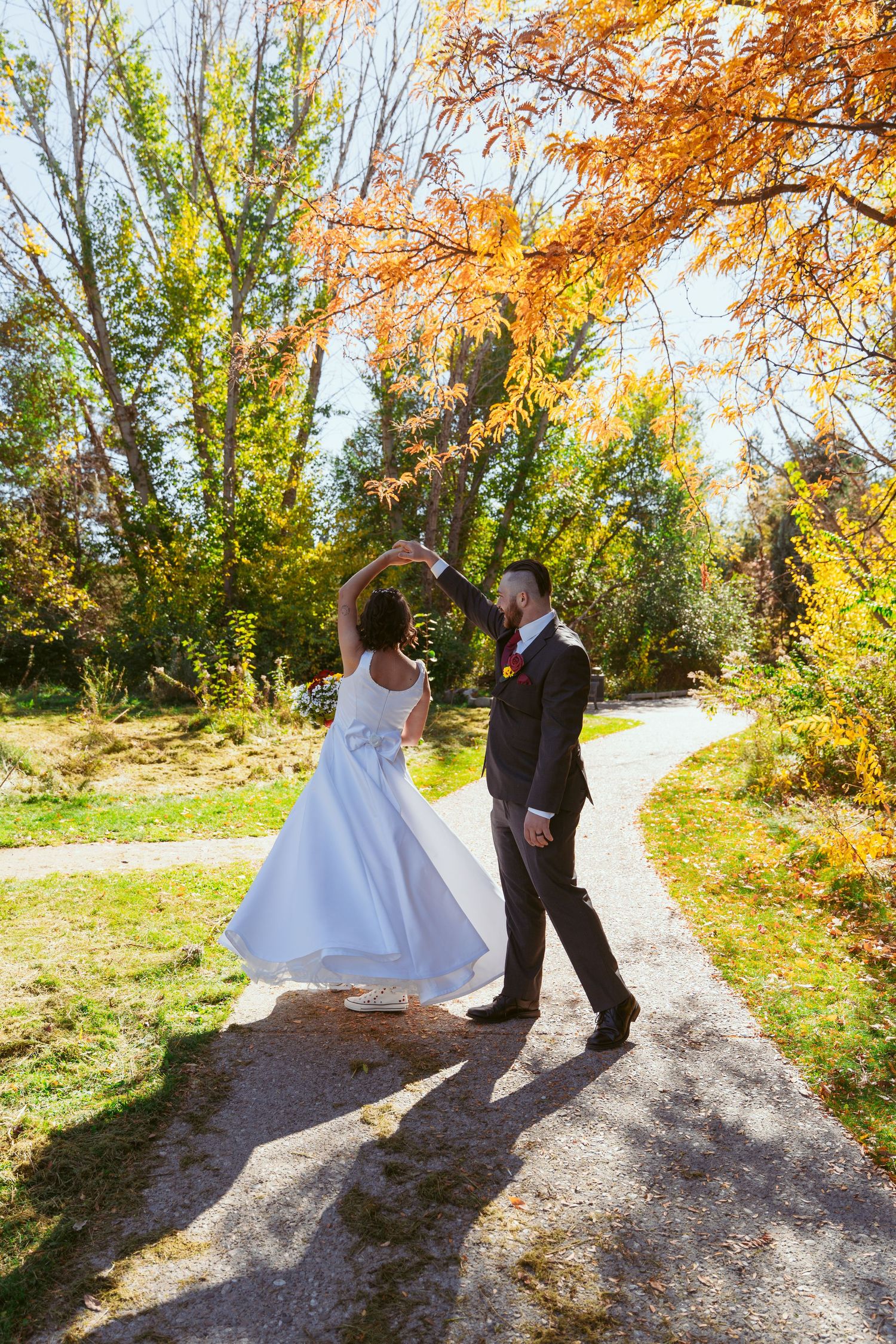Couple dances on autumn path surrounded by golden fall foliage.