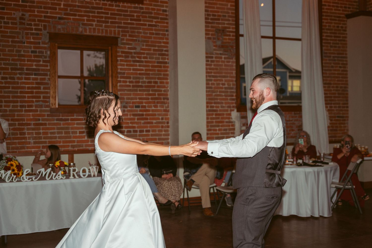 Wedding couple performs dance moves in an elegant brick-walled reception venue.