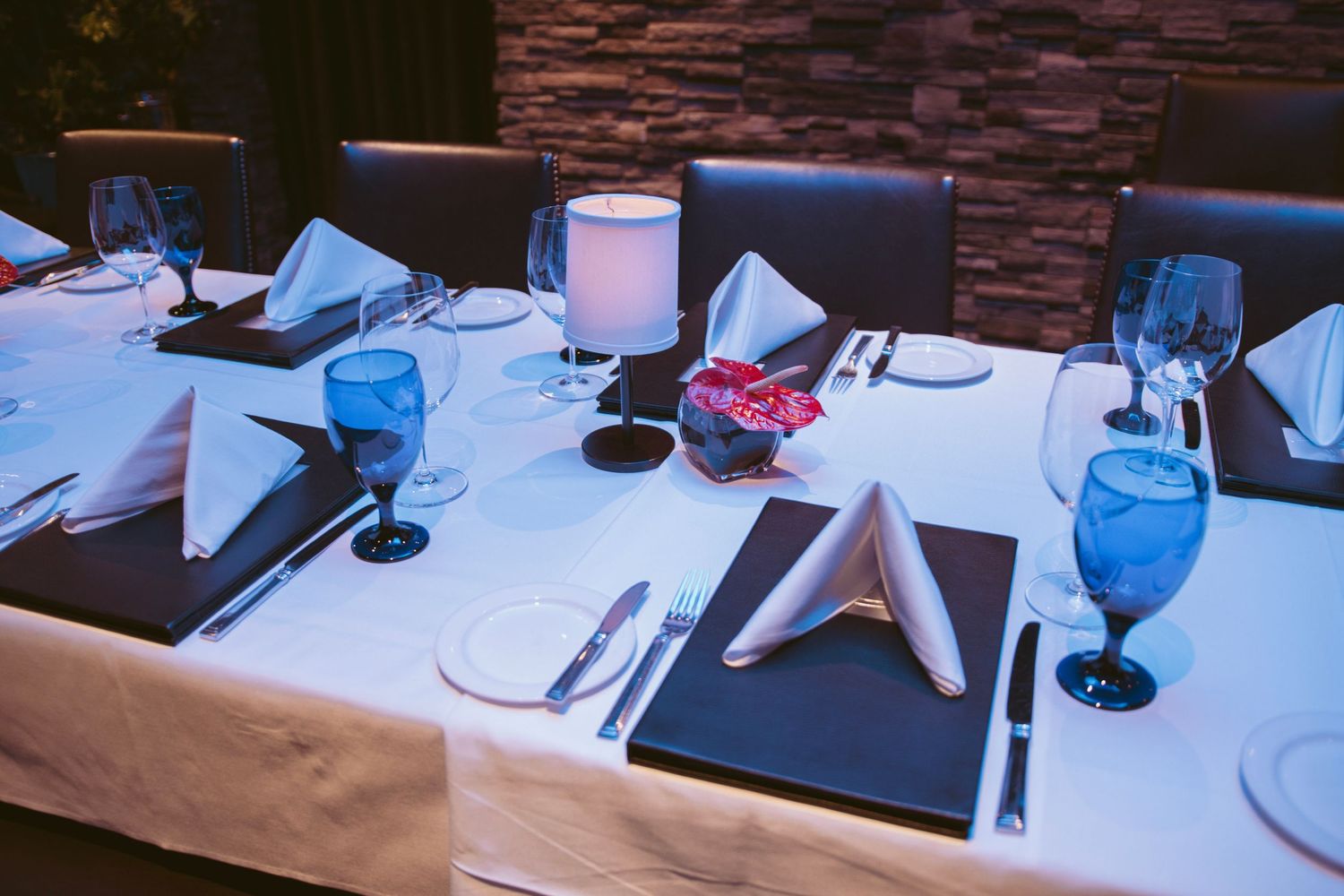 Formal place settings with blue glassware and white linens on dark tables.