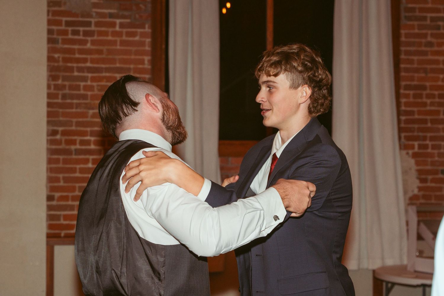 Wedding guests embracing during a dance in a rustic brick venue.