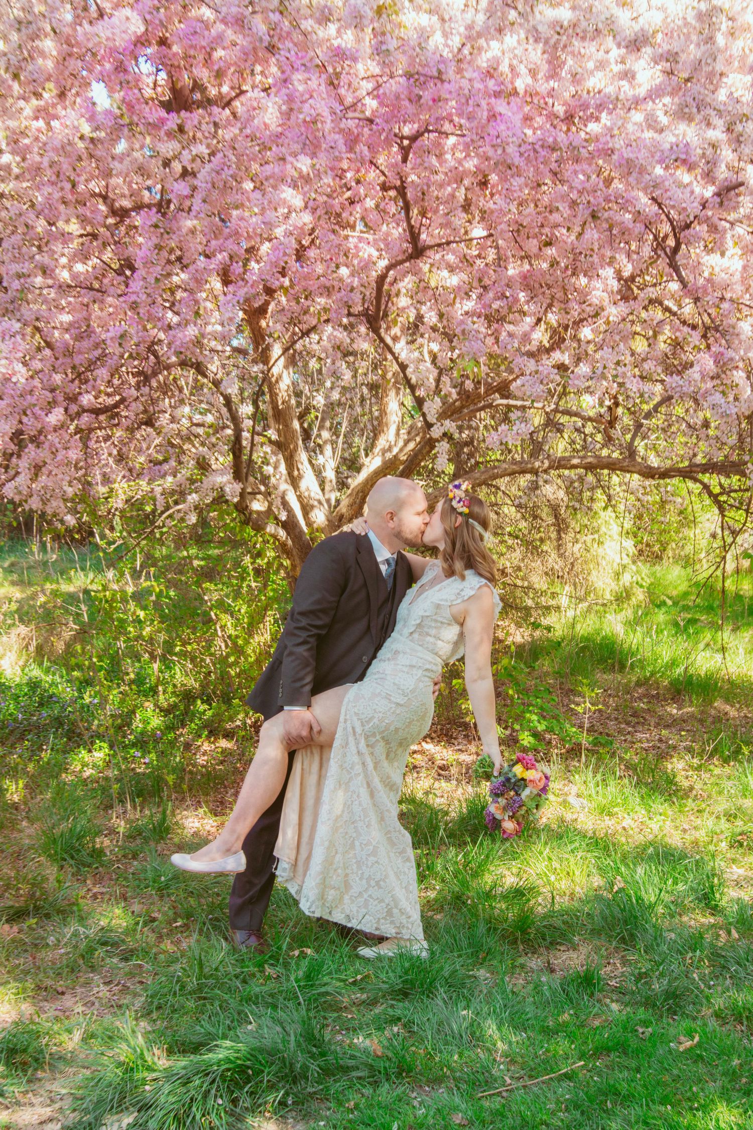 Couple shares romantic moment under blooming cherry blossom trees on grassy lawn.