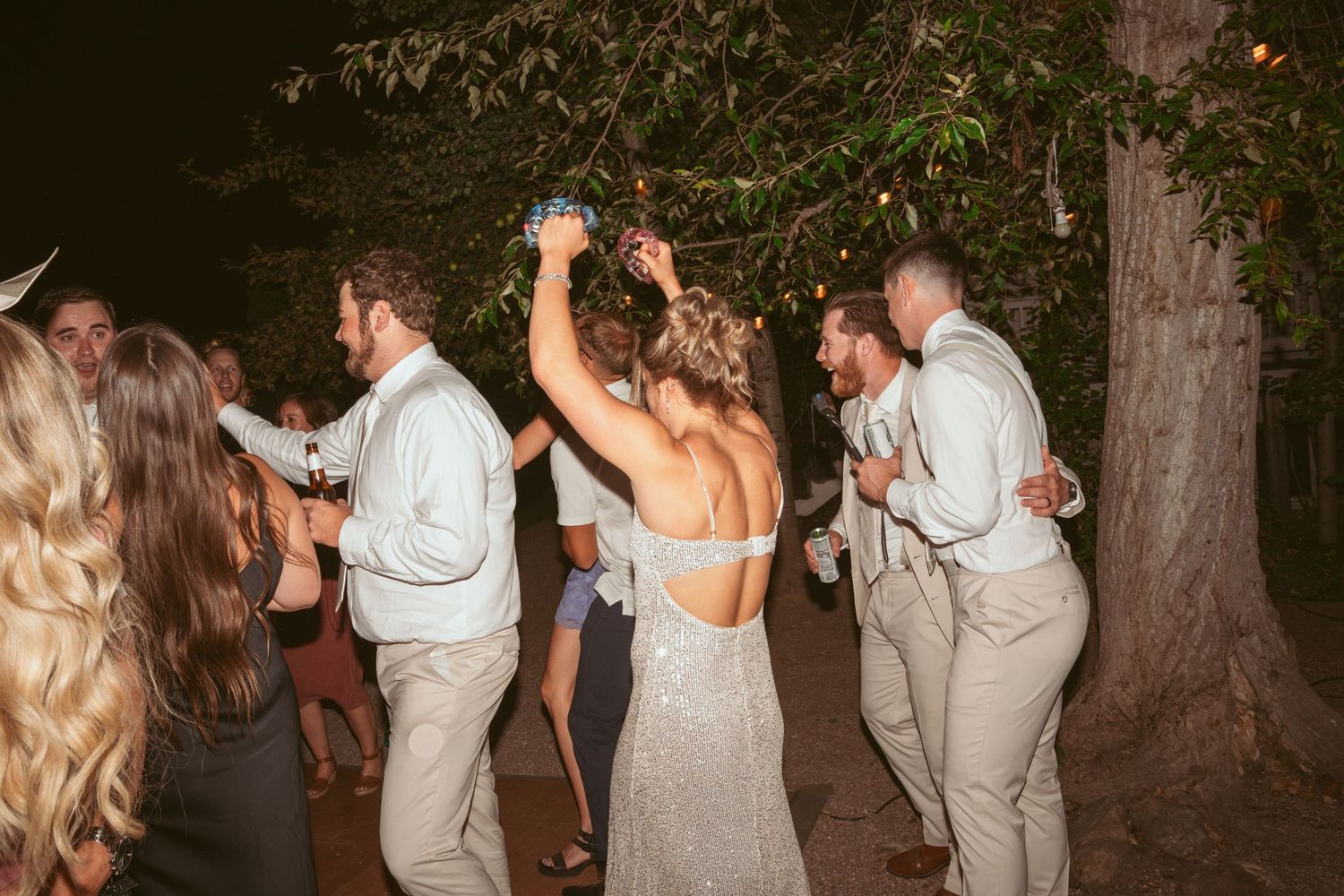 Wedding guests dancing outdoors under trees at a nighttime reception celebration.