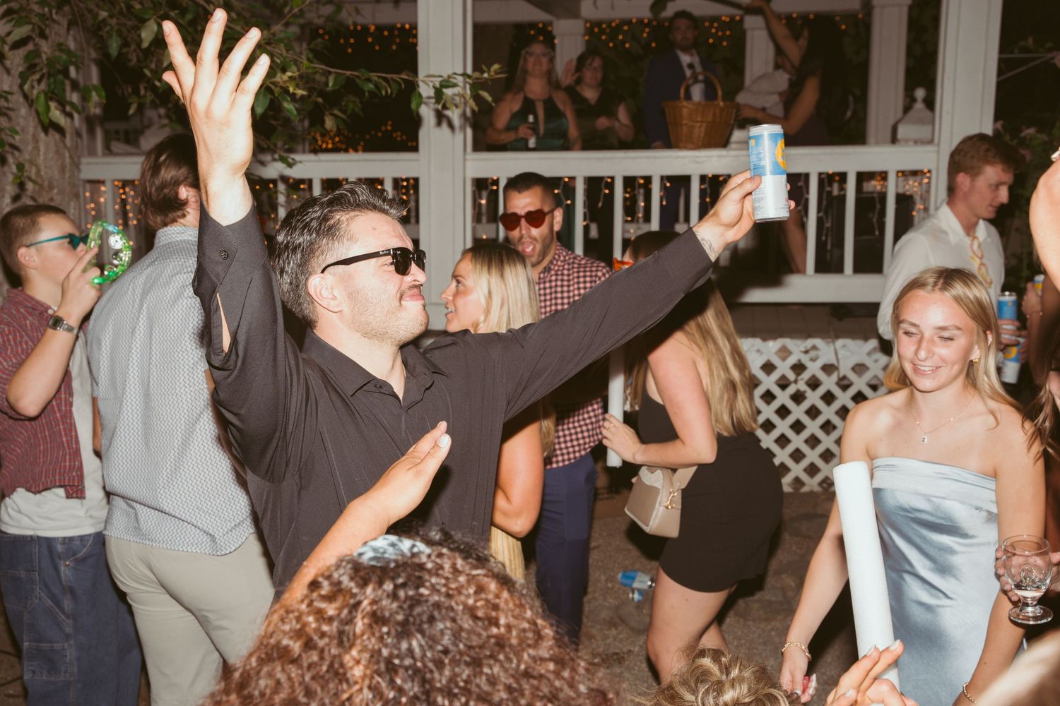 Energetic party guests dancing and having fun at a lively wedding reception with white lattice decor.
