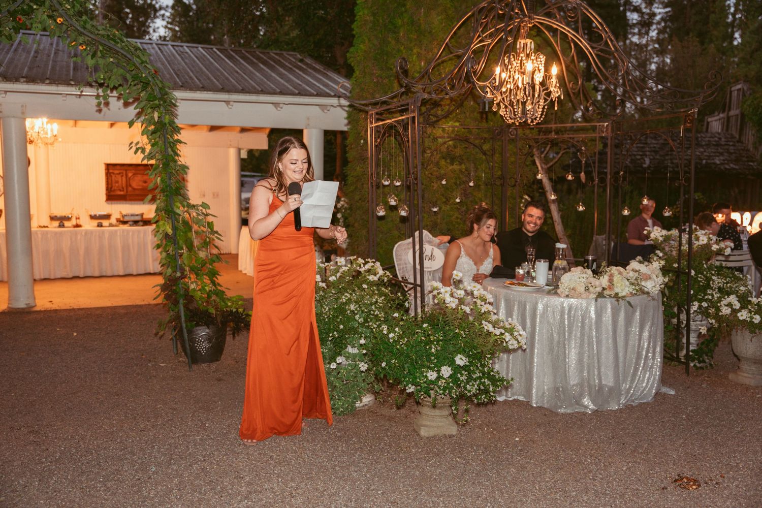 An outdoor wedding reception with a person in orange dress standing near decorated dining tables.