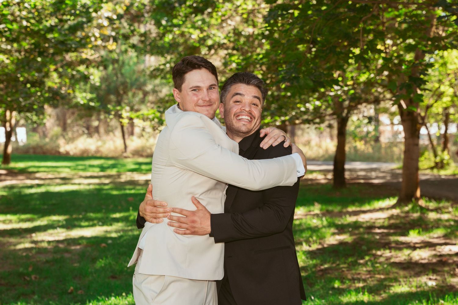 Two people embrace in a sunlit garden setting during what appears to be a special celebration or event.