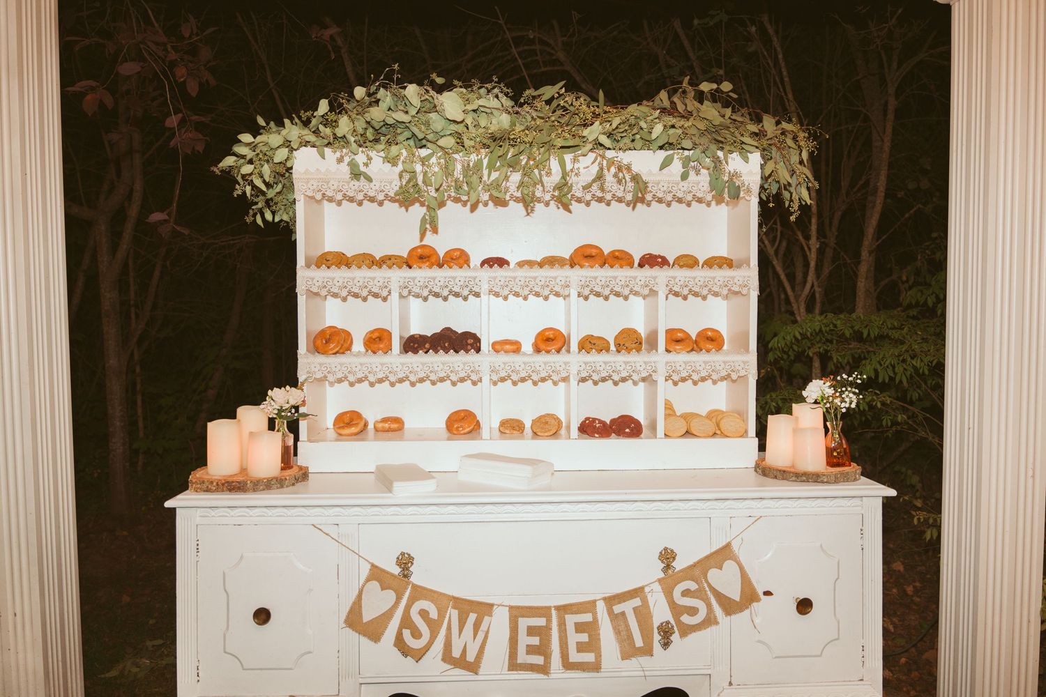 Elegant dessert display table with multiple tiers of treats and 'Sweet' banner at wedding reception.