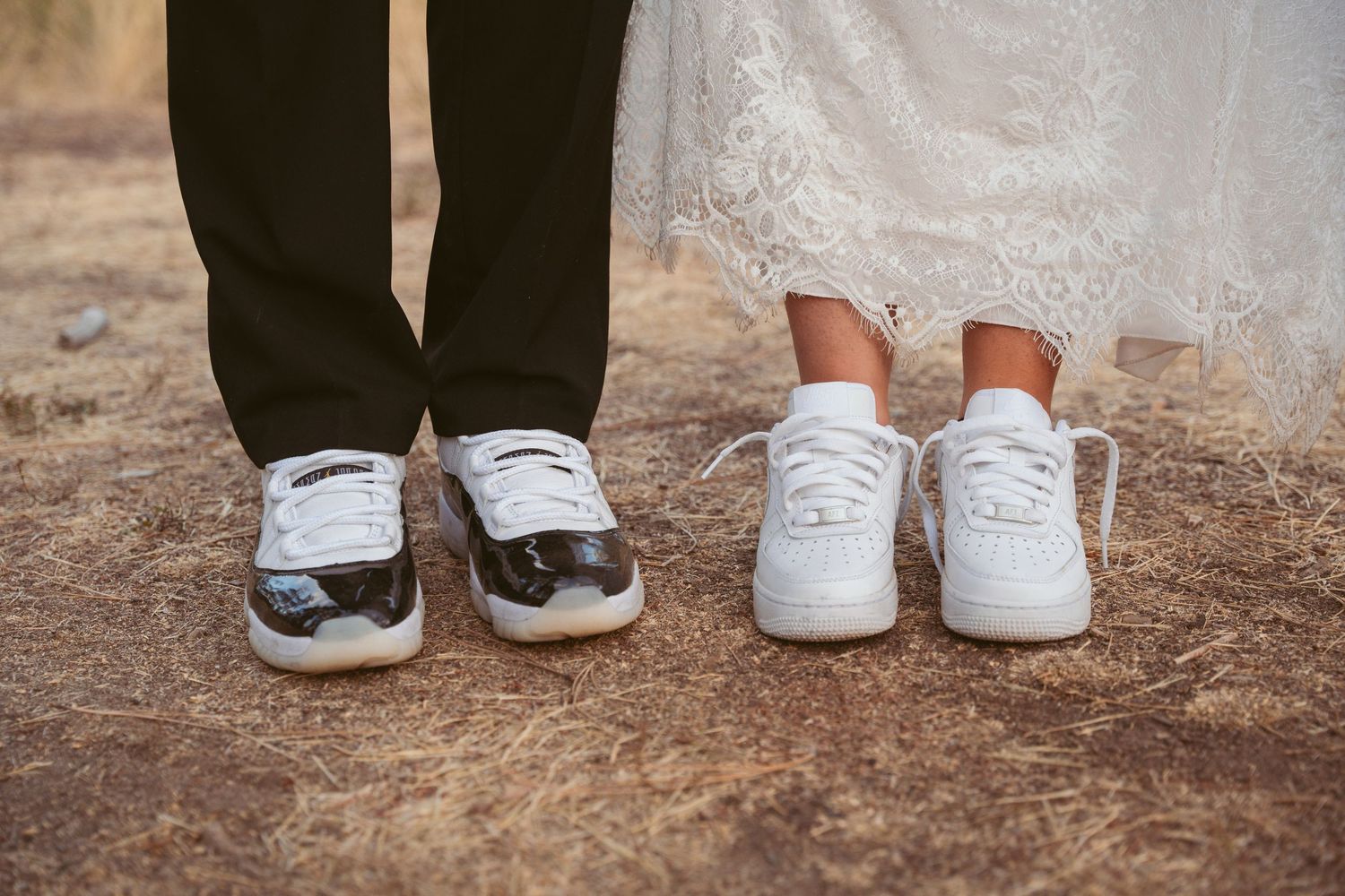 A line of matching white sneakers worn by wedding party members on a rustic ground.