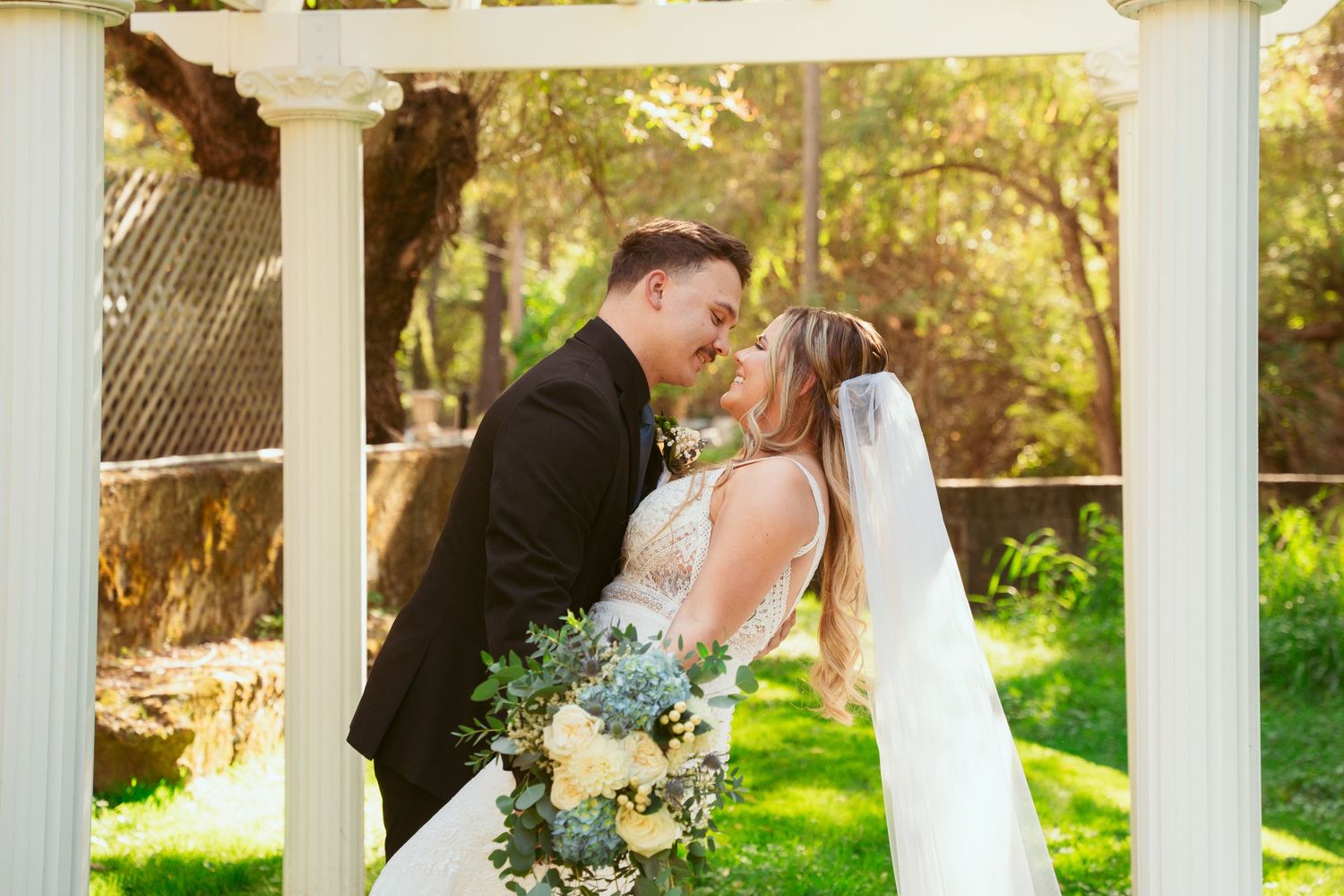 Elegant wedding ceremony setup under white pillars with natural sunlight streaming through.