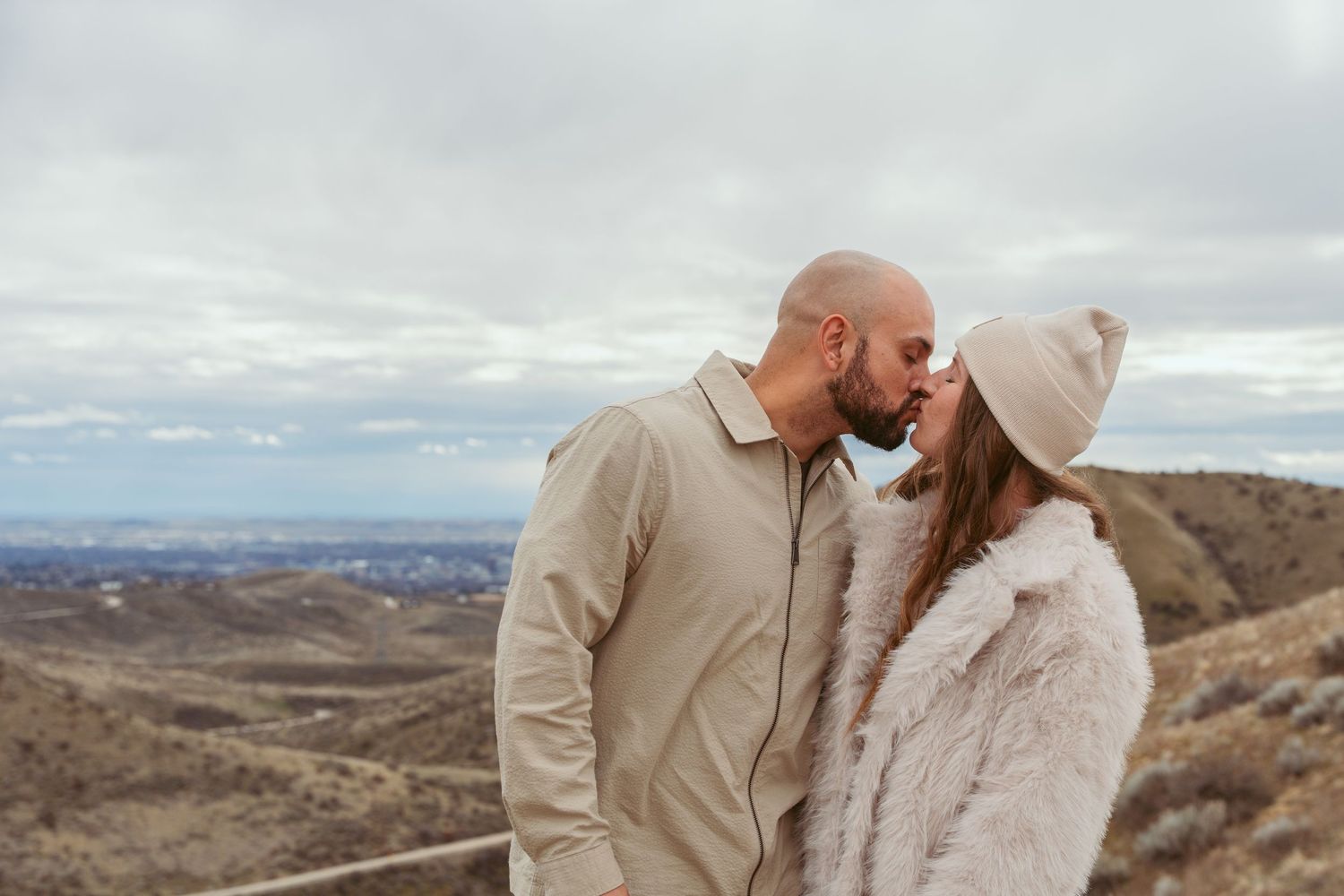 A couple in warm winter attire sharing romantic moments against a scenic mountain landscape backdrop.
