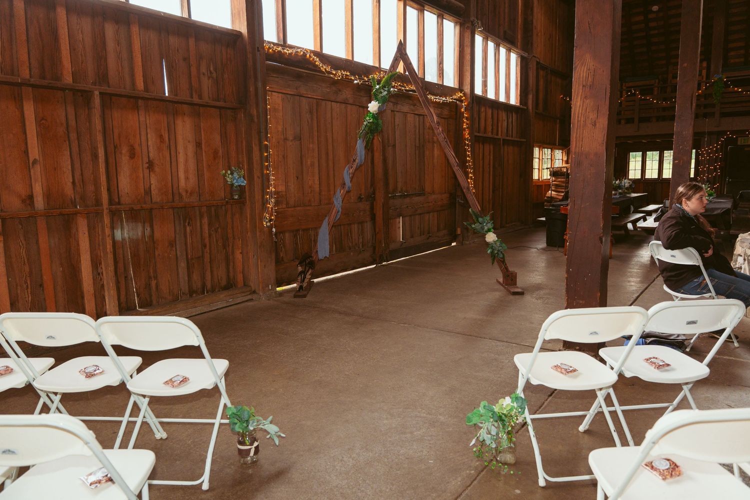 Wooden barn interior with white folding chairs set up for a wedding ceremony.