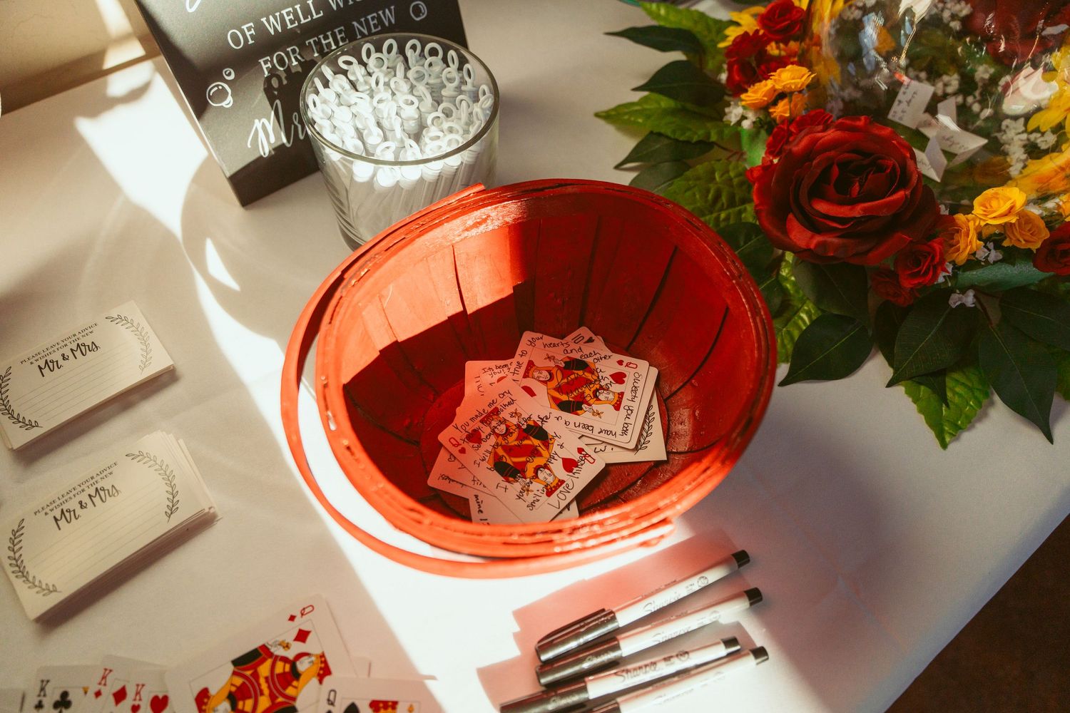 Wedding reception table decorated with red roses, playing cards and glassware.