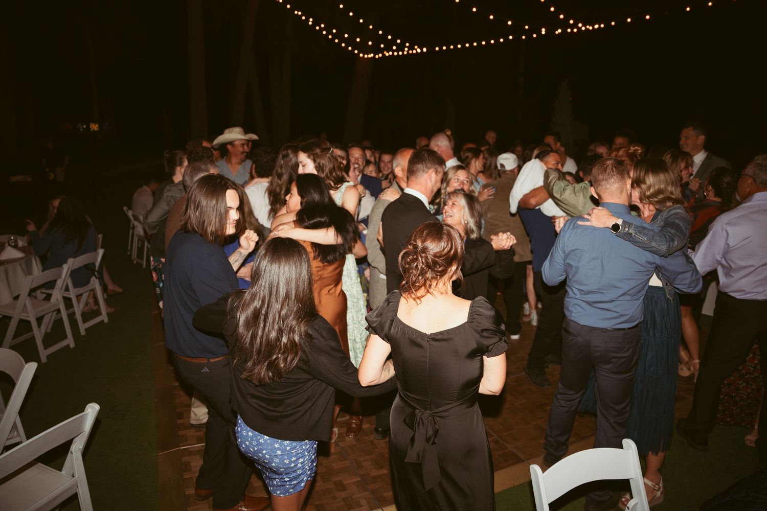 Guests dancing and mingling at a nighttime outdoor celebration with overhead string lights.