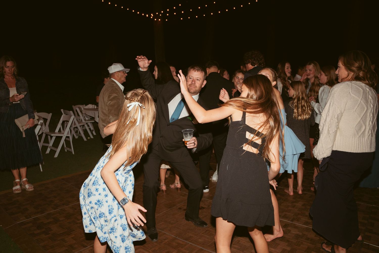 Guests dancing and socializing at an outdoor evening party under decorative lighting.