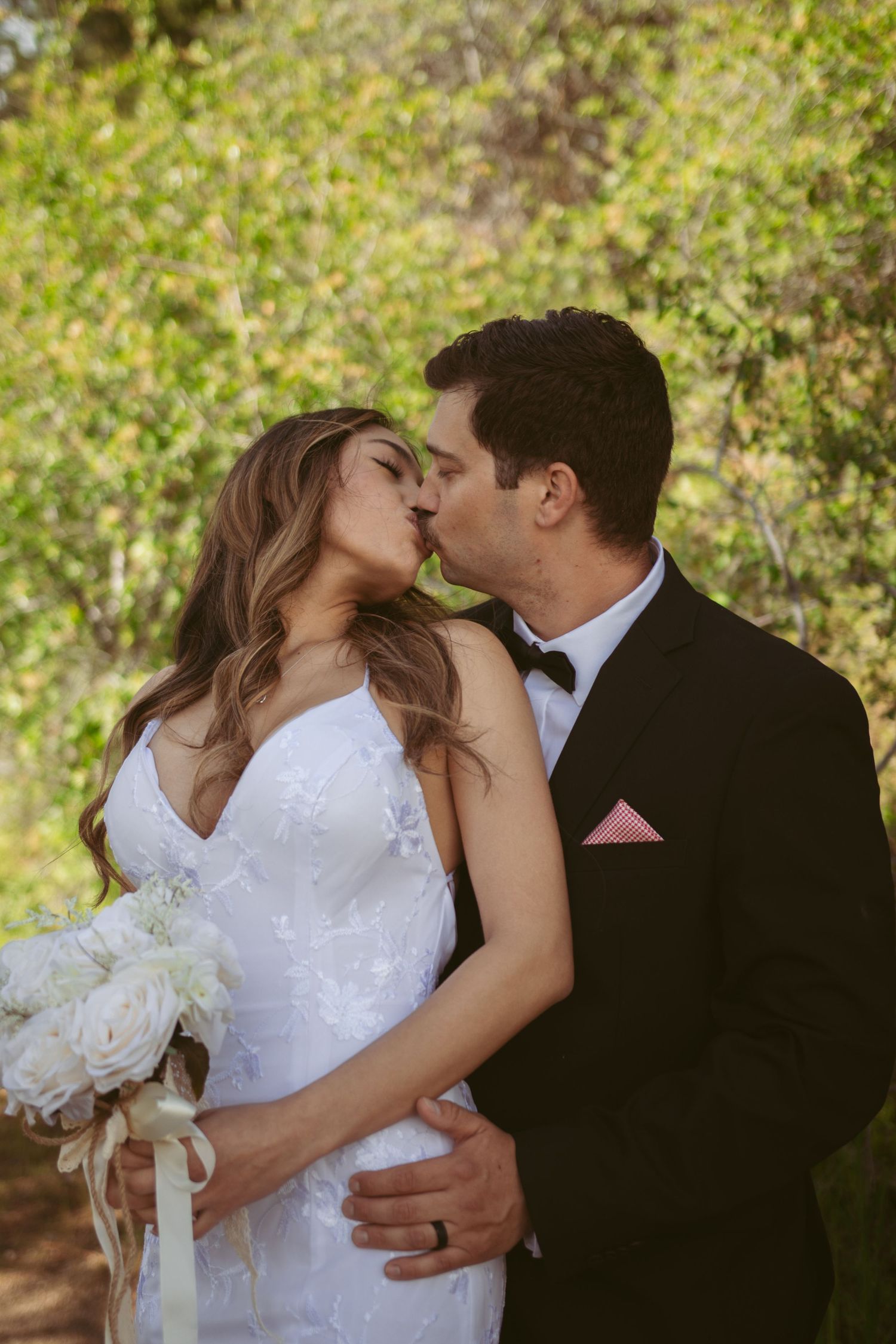 A romantic wedding moment captured with a white bouquet against a natural outdoor setting.