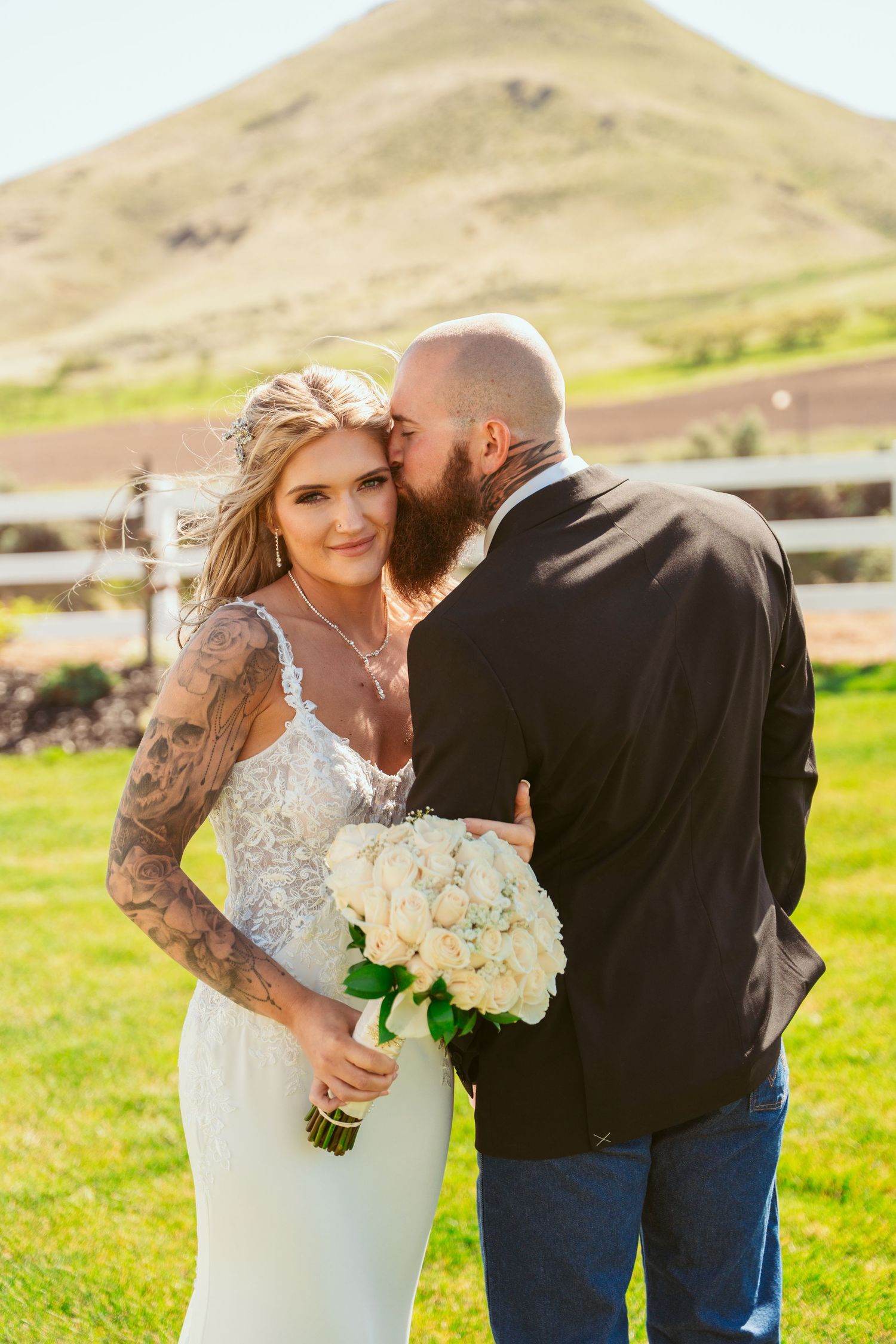A romantic wedding couple shares intimate moments in a sunny field with white flowers and mountain views.