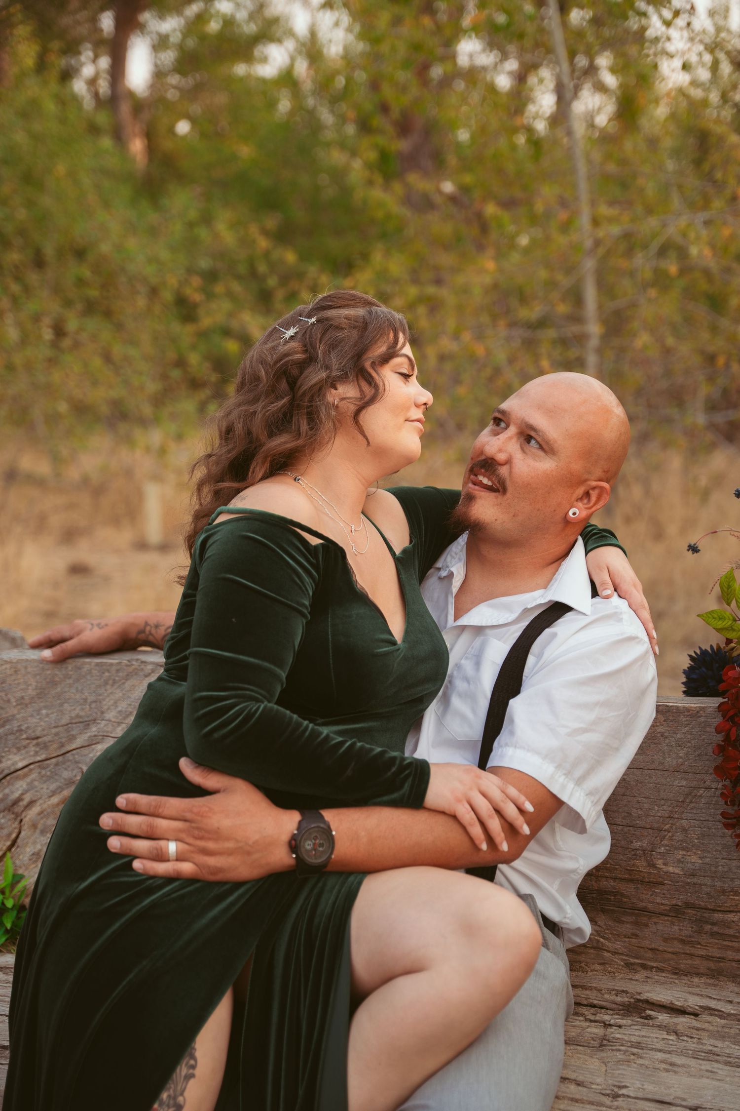 Couple shares playful moments while posing on a fallen log in an autumn outdoor setting.