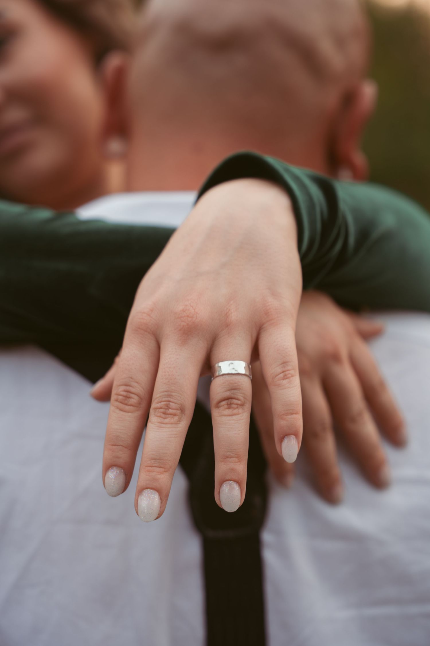 Close-up shot of hands with an engagement ring against a white shirt background.