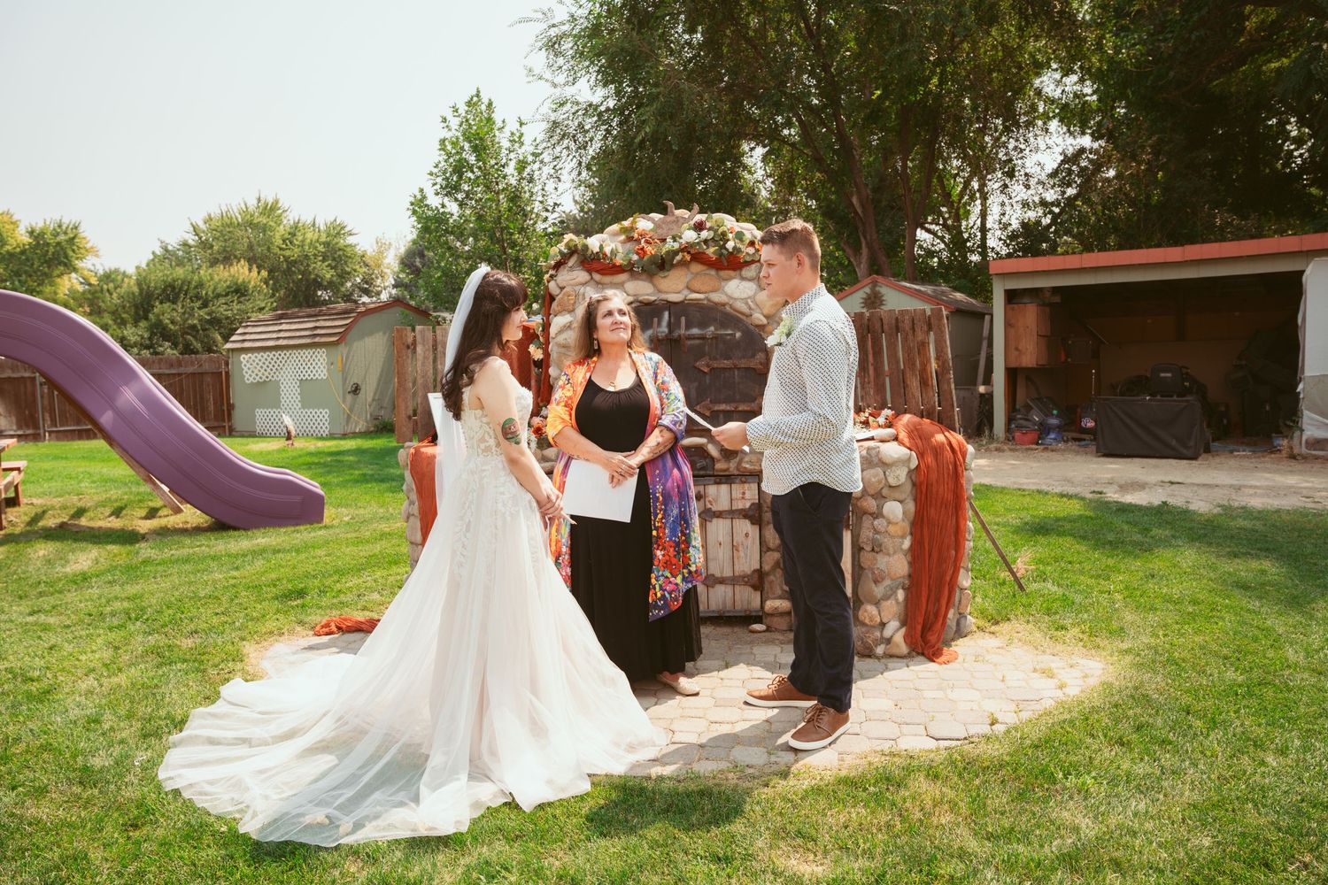 A couple dances outdoors in a garden setting with decorative stone walls and greenery.