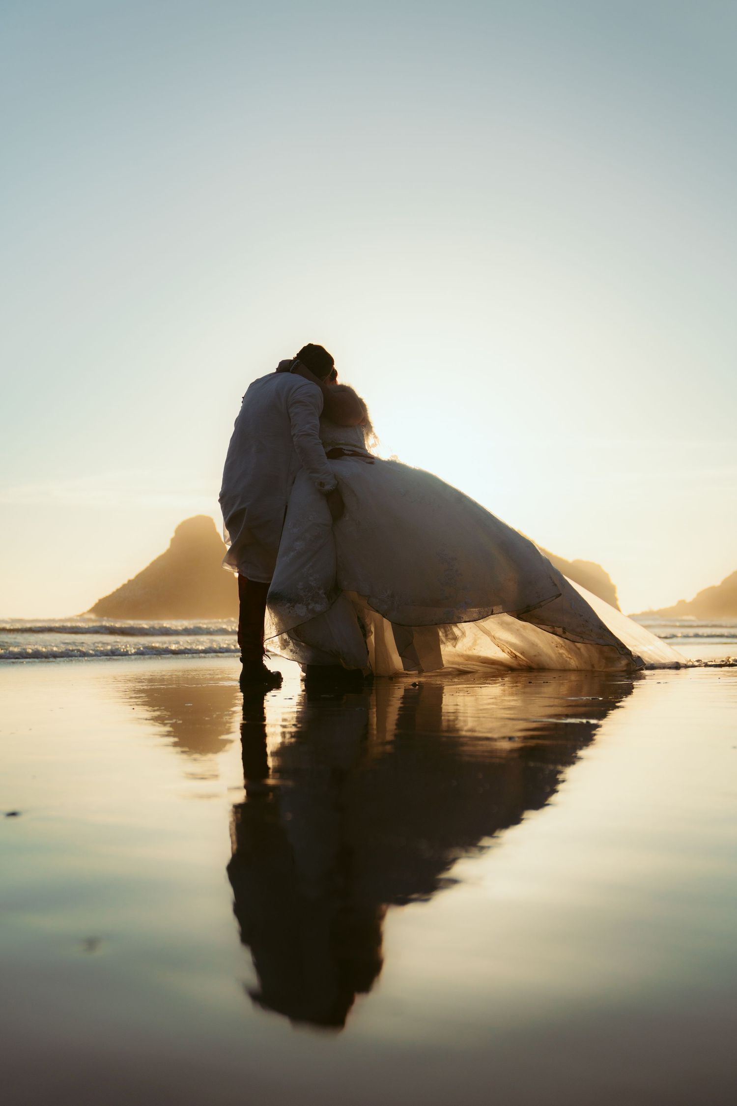 Artistic beach photography with couple's reflection in wet sand during sunset.