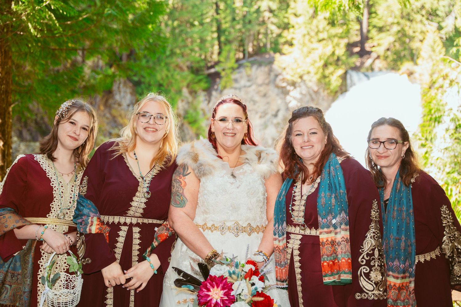 Wedding guests in renaissance-inspired attire pose together in front of forest greenery.