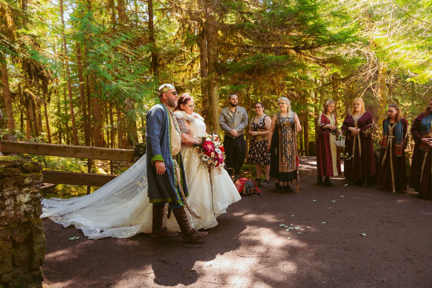 Romantic forest wedding ceremony with guests gathered under tall evergreen trees.
