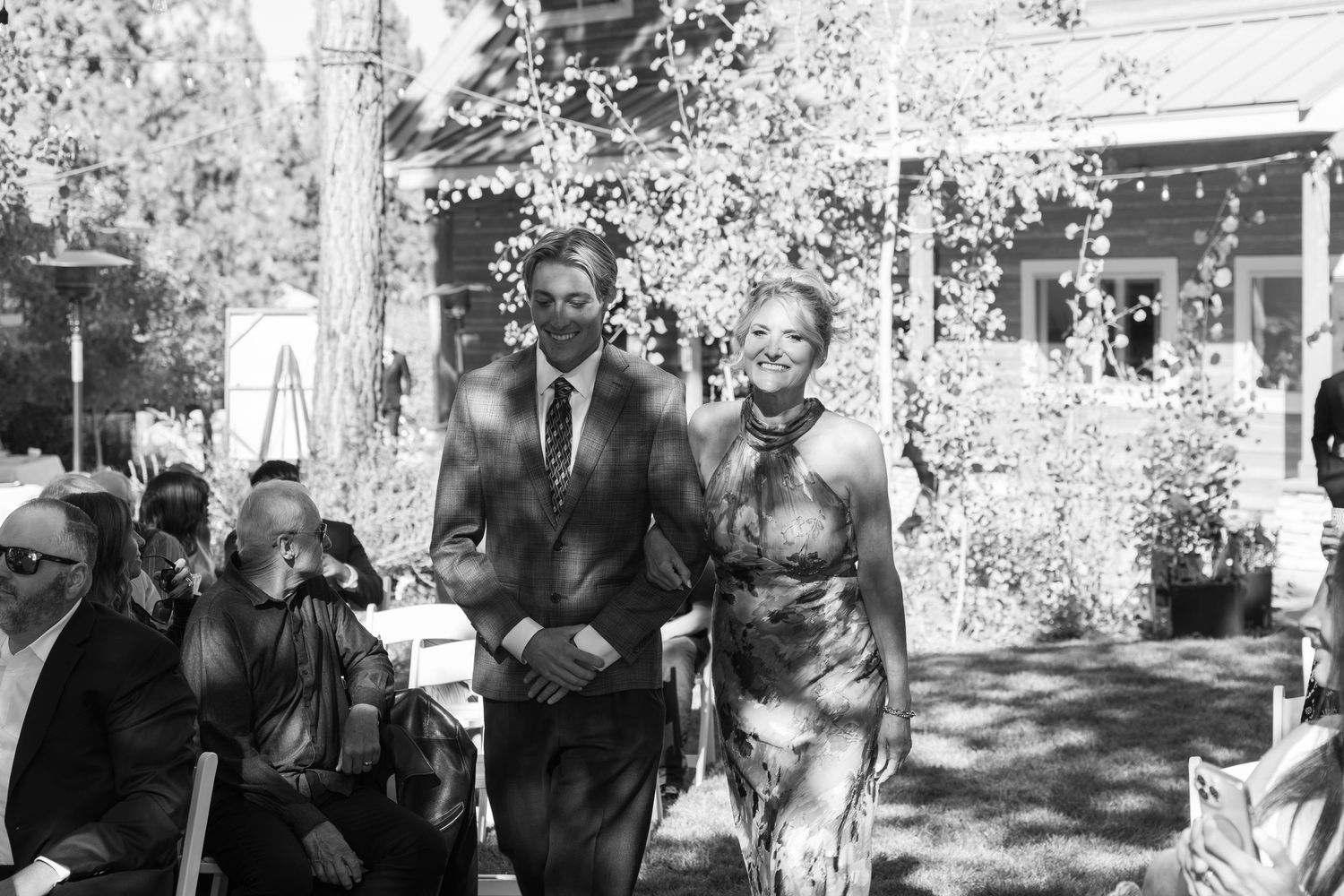 Black and white photo of wedding processional on a tree-lined outdoor path.
