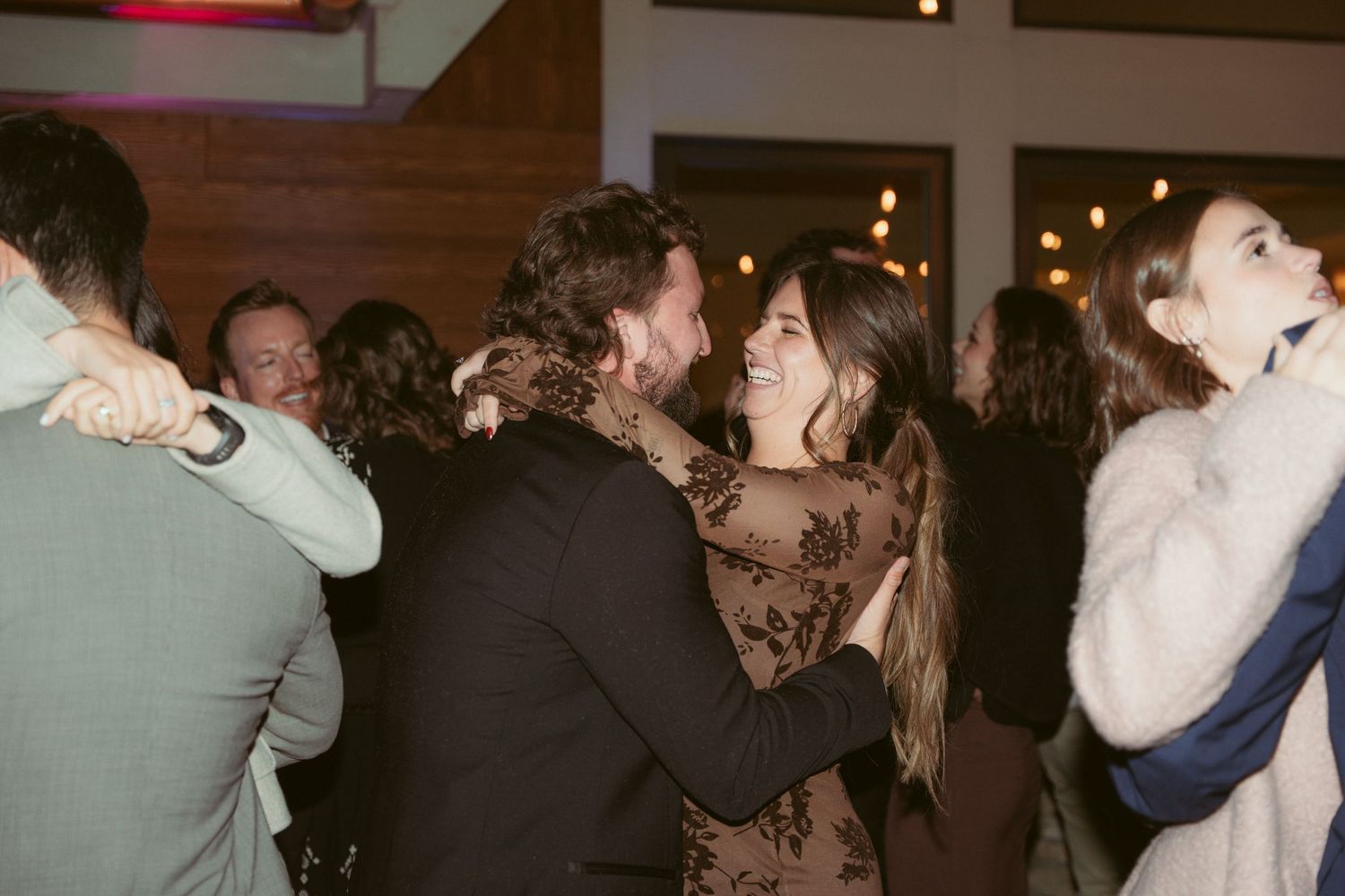 Couples dancing and embracing at an indoor wedding reception with warm lighting and festive atmosphere.