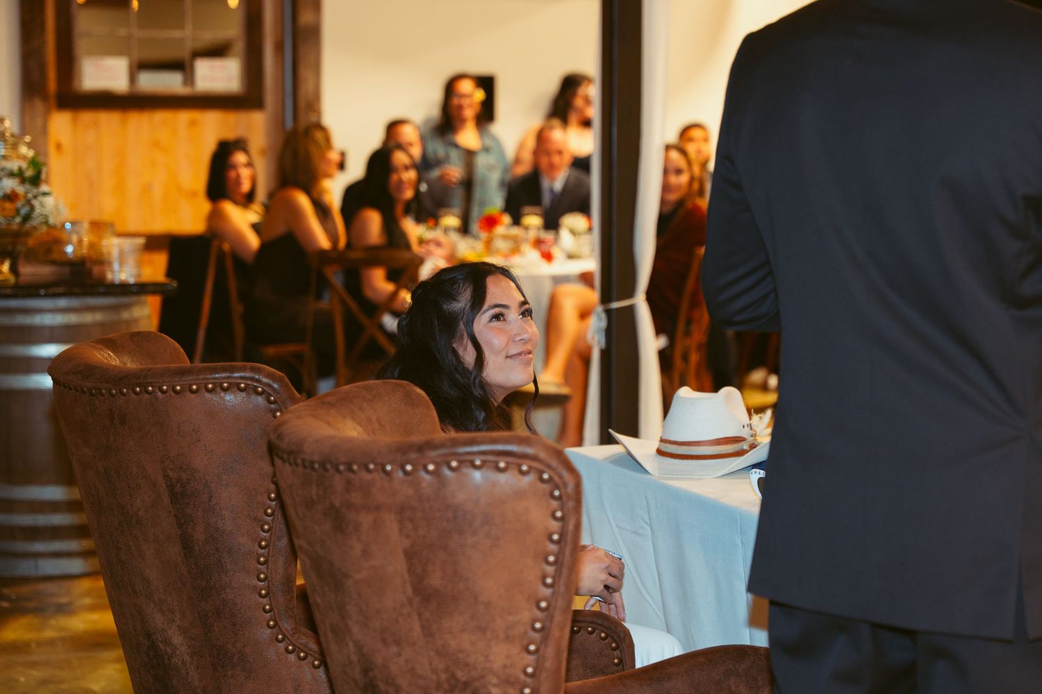 Elegant wedding reception setup with brown leather chairs and white tablecloths in a cozy indoor venue.
