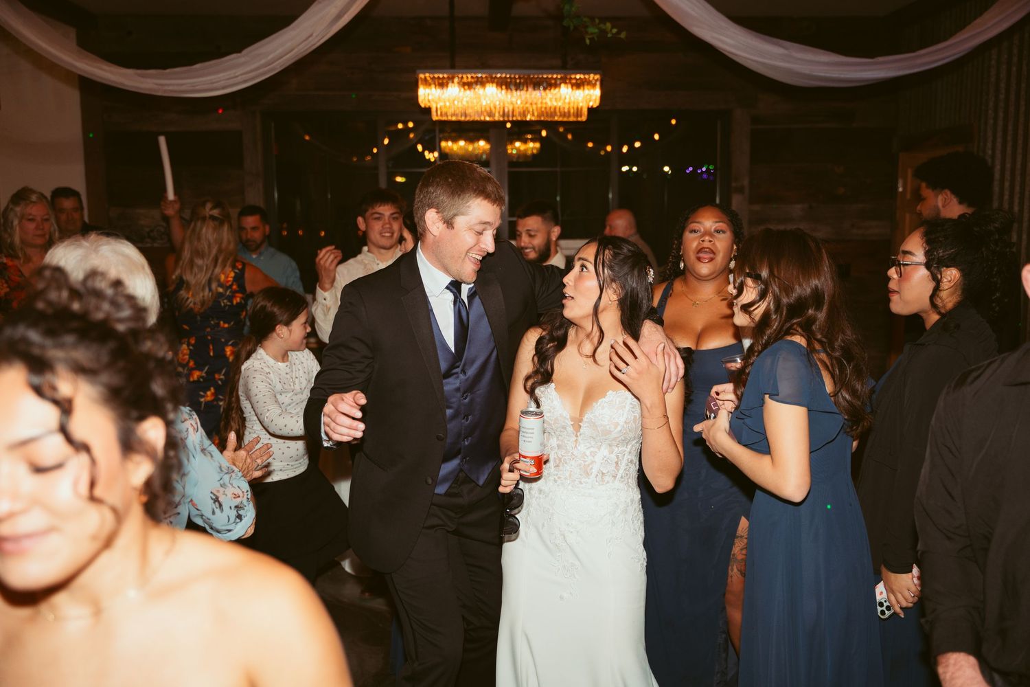 Guests socializing and dancing at a formal event in a venue with string lights and dark decor.