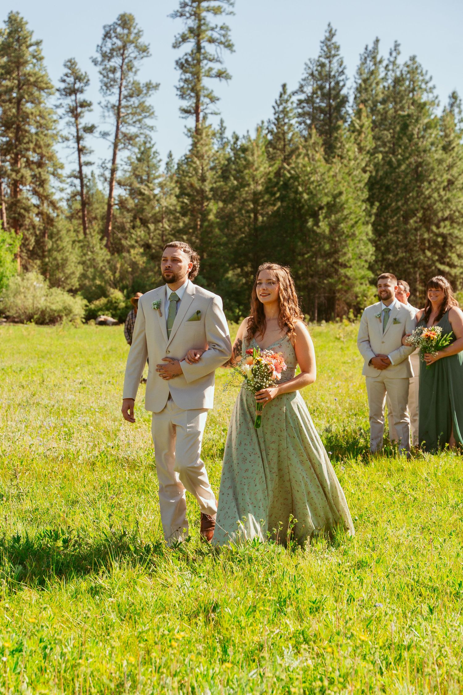Wedding party in tan suits and mint green dresses walking through a sunny meadow.