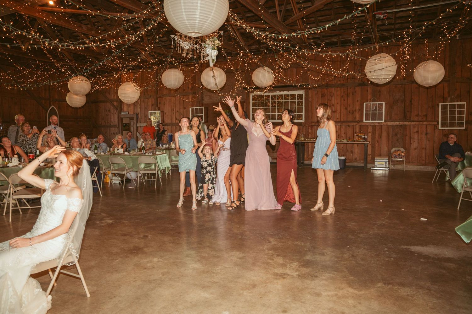 Wedding reception dance floor scene with string lights and paper lanterns decorating a wooden barn ceiling.