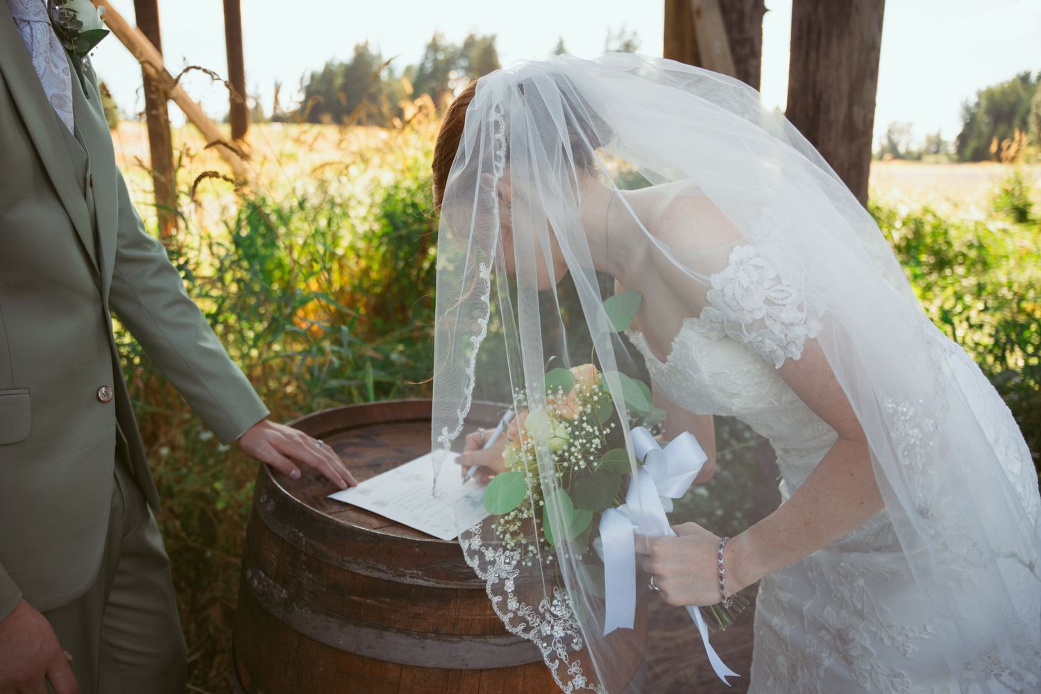 Close-up of couple signing wedding documents on wooden barrel during outdoor ceremony.