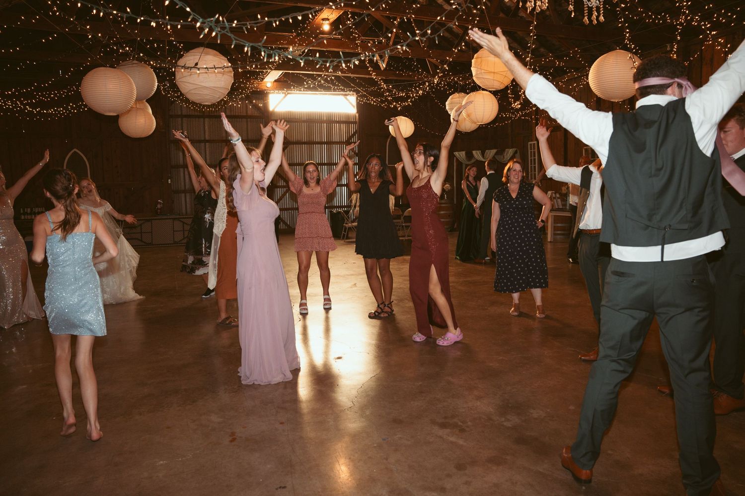 Lively dance floor scene at a wedding reception with string lights and paper lanterns overhead.