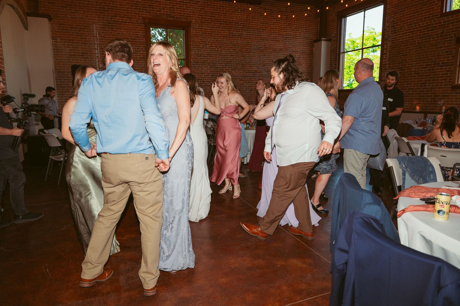 Wedding guests dance and socialize in a rustic venue with exposed brick walls.
