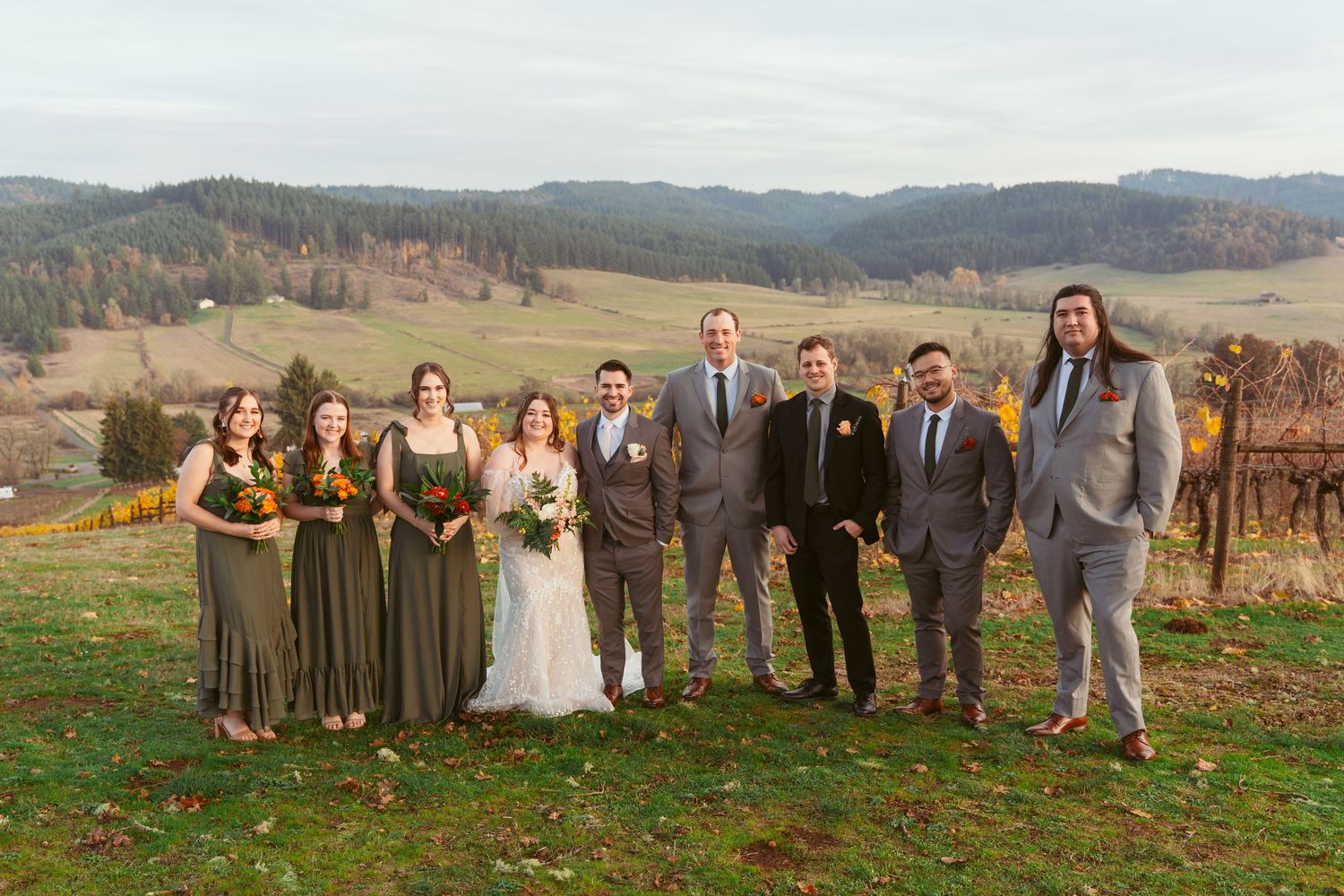 Wedding party poses together on a scenic hillside with mountains and autumn colors in the background.