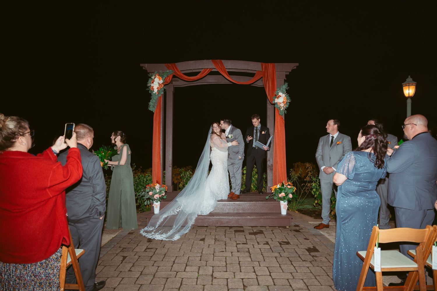 Red-draped wedding arch decorated with floral arrangements for an evening outdoor ceremony.