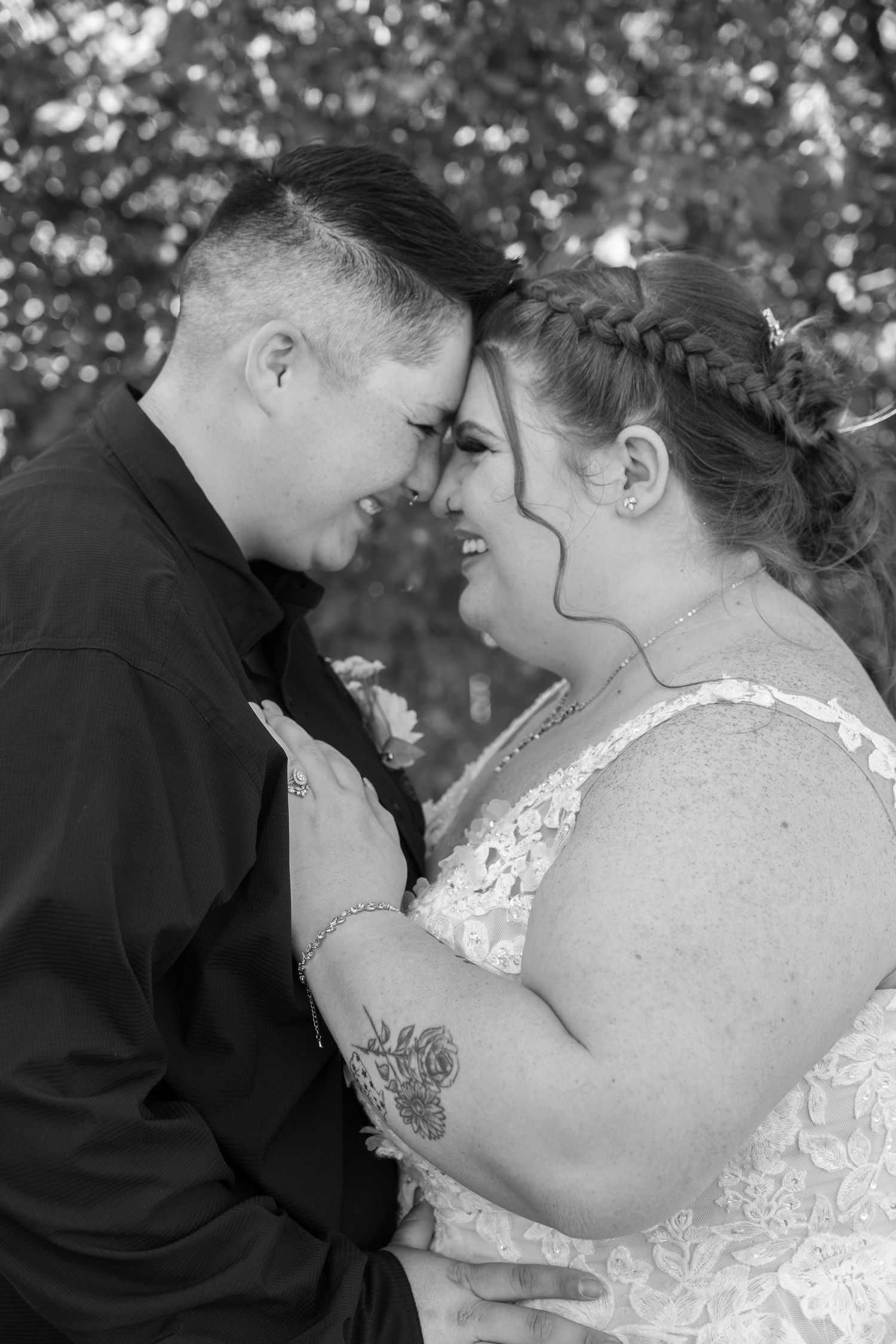 A tender black and white wedding portrait shows a couple in an intimate moment with their foreheads touching outdoors.