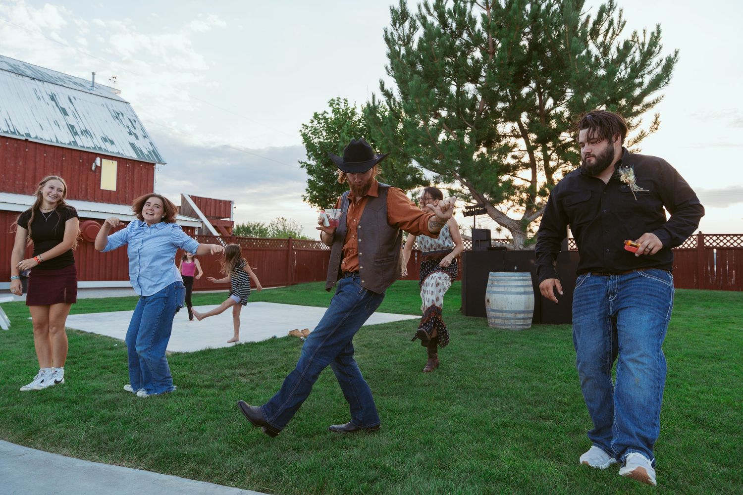 Group dancing on a grassy lawn at dusk with a red barn visible in the distance.