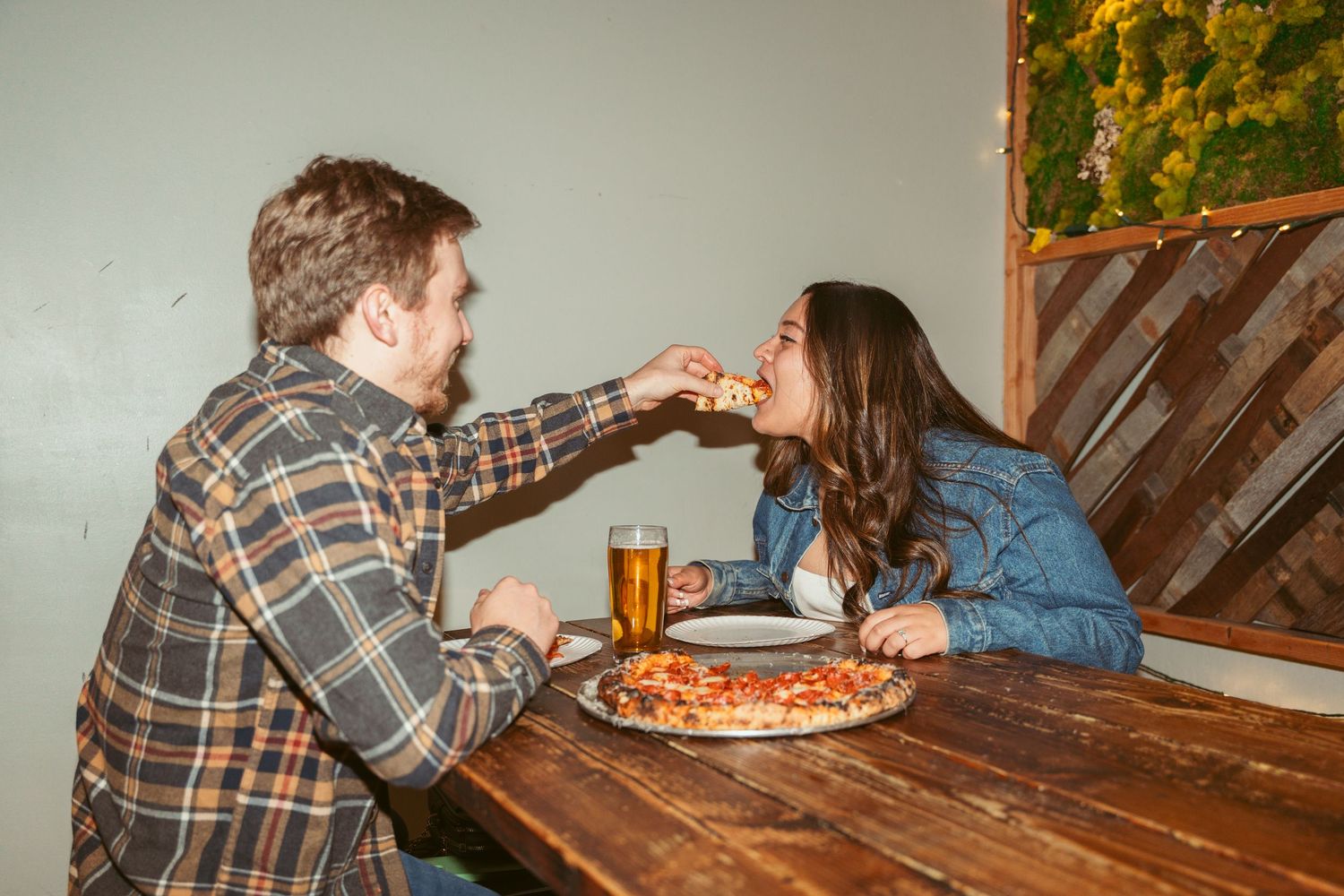 Two people enjoying pizza and conversation at a wooden table in a casual dining setting.