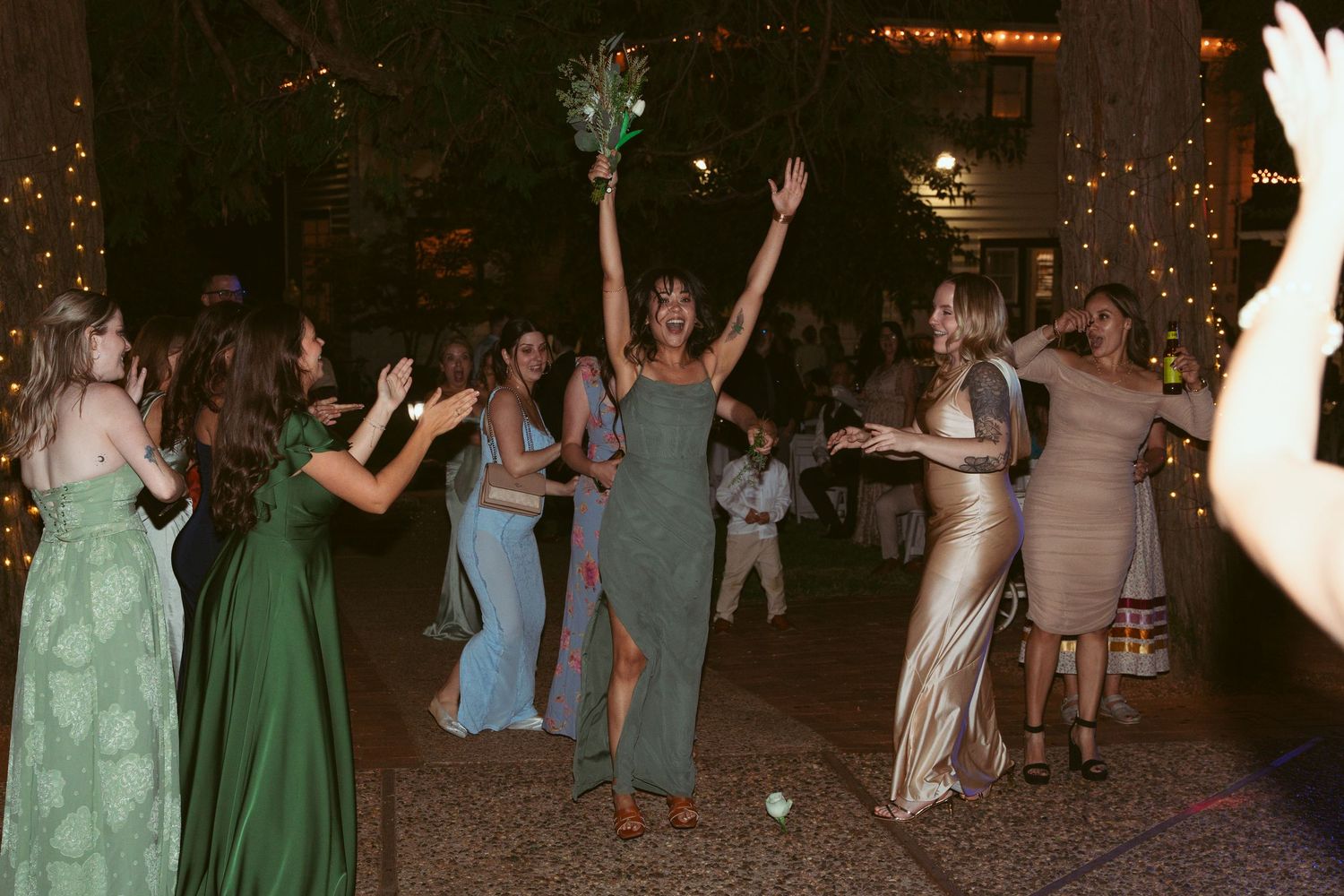 Wedding guests dancing together outdoors at night with decorative lights in the background.