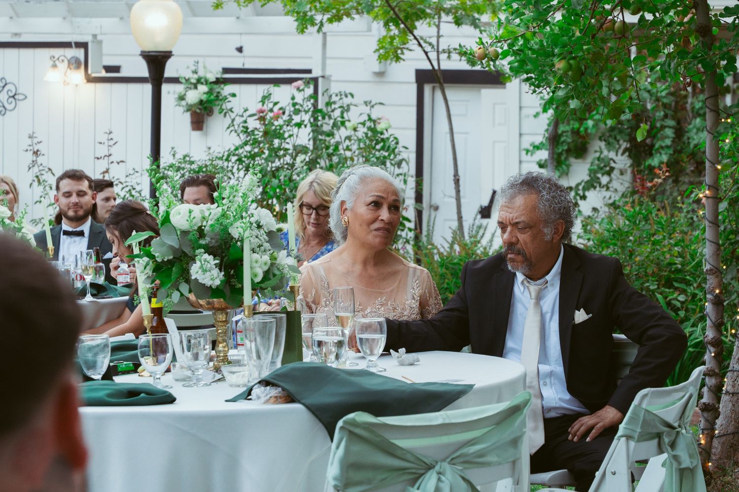 Wedding guests enjoy an elegant outdoor dinner reception with green floral decorations.
