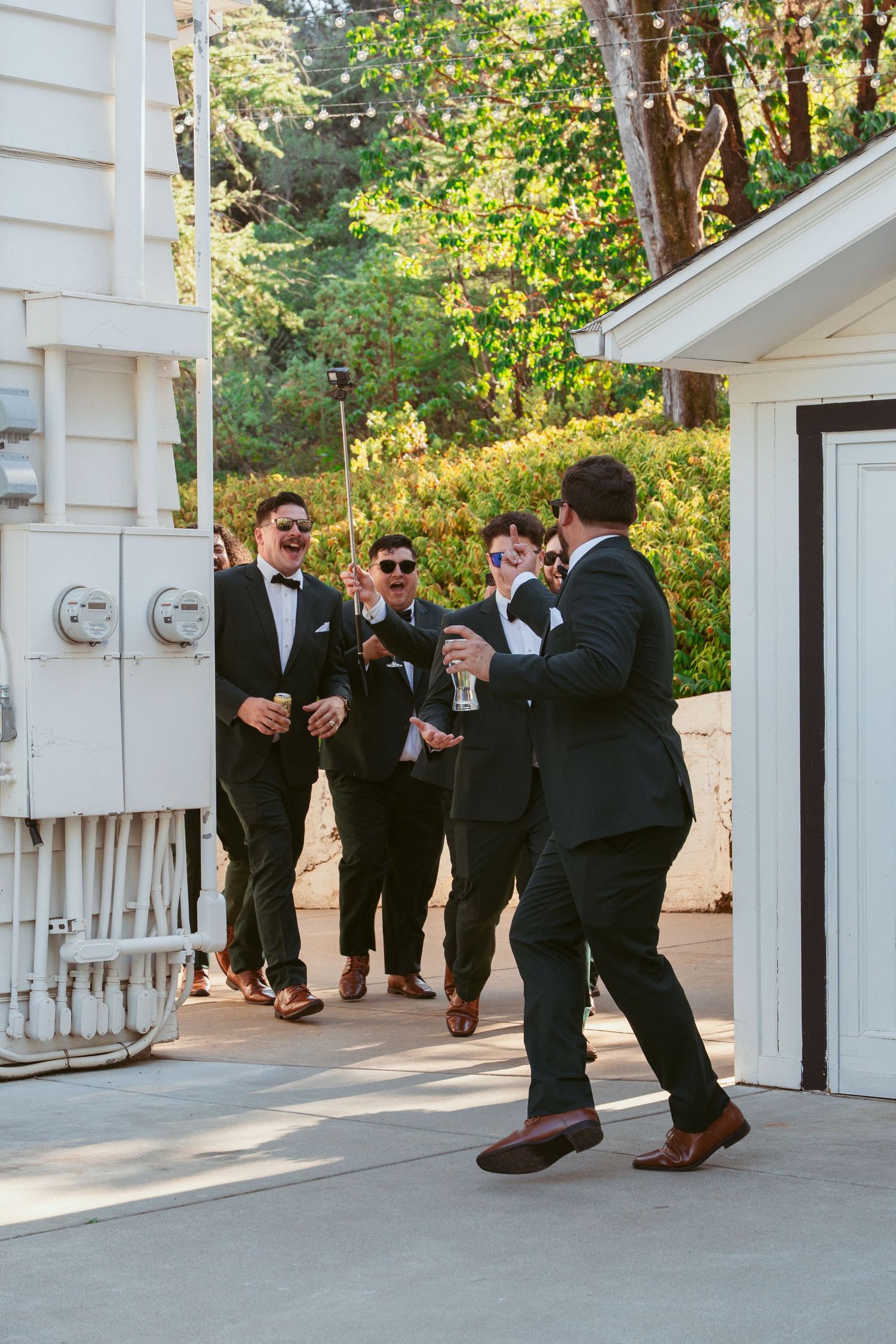 Groomsmen in black tuxedos gathered on a white porch during wedding celebrations.