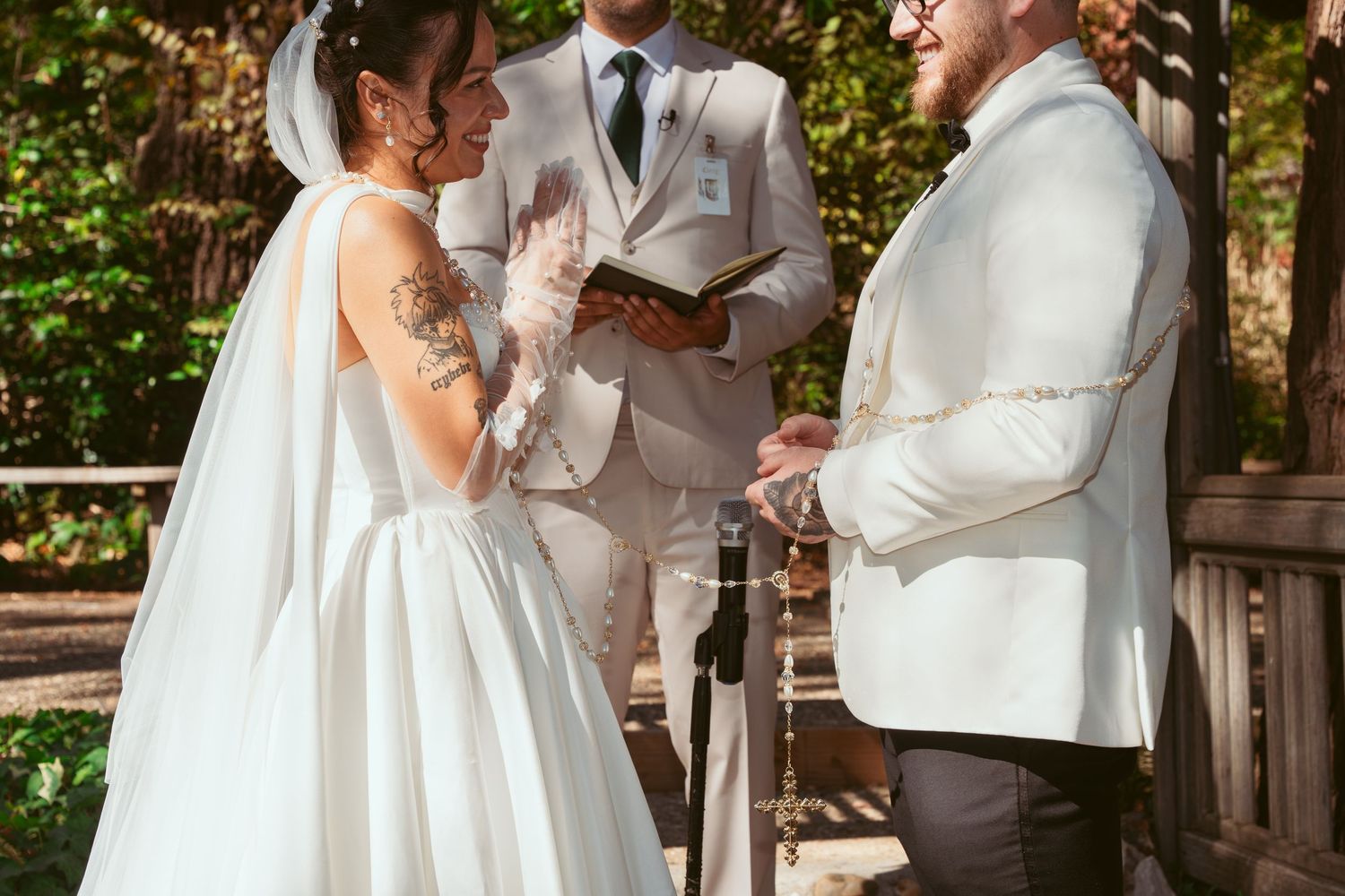 Wedding party gathered under wooden pergola in outdoor garden setting with white and neutral attire.