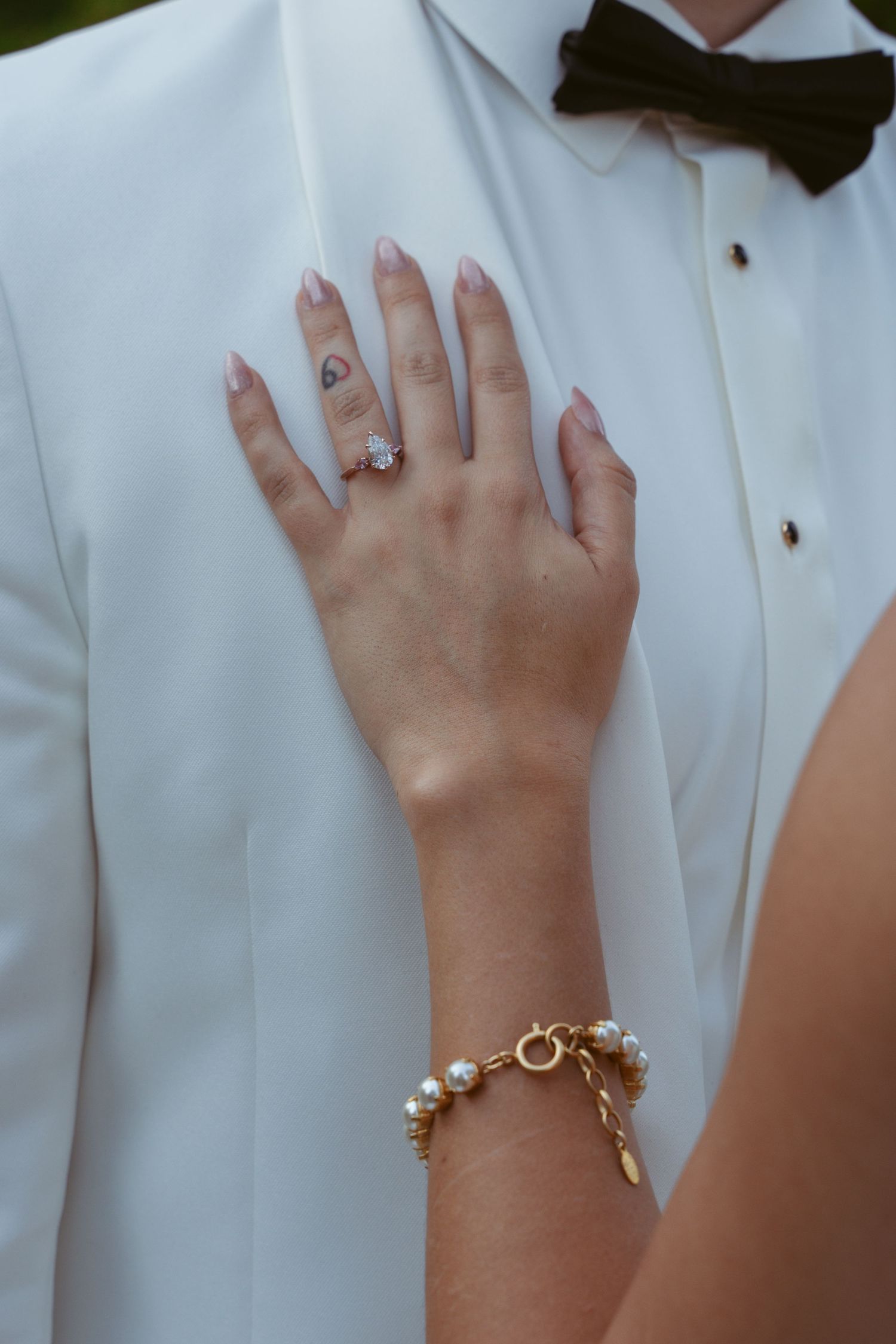 Close-up view of hands wearing engagement rings against a white formal attire background.