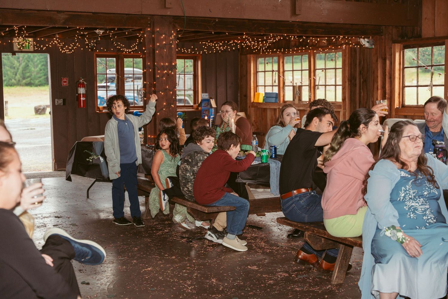Wedding guests enjoying reception festivities inside wooden barn with natural lighting.