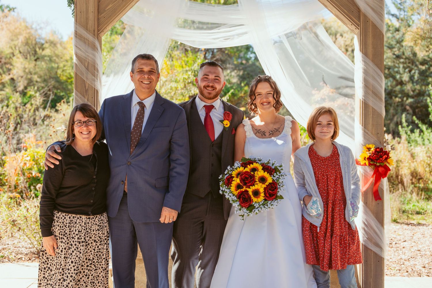 Family wedding portrait under rustic wooden pavilion with white draping and fall floral decorations.
