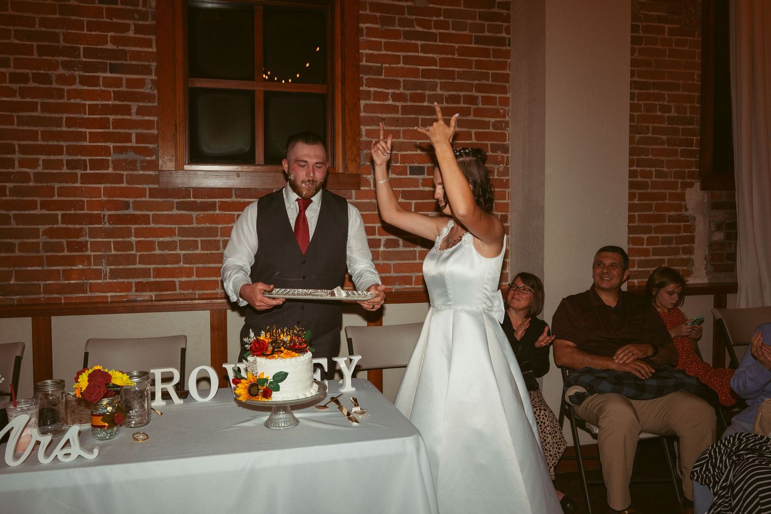 Wedding reception celebration with guests dancing in front of a decorative Mr & Mrs sign on brick walls.