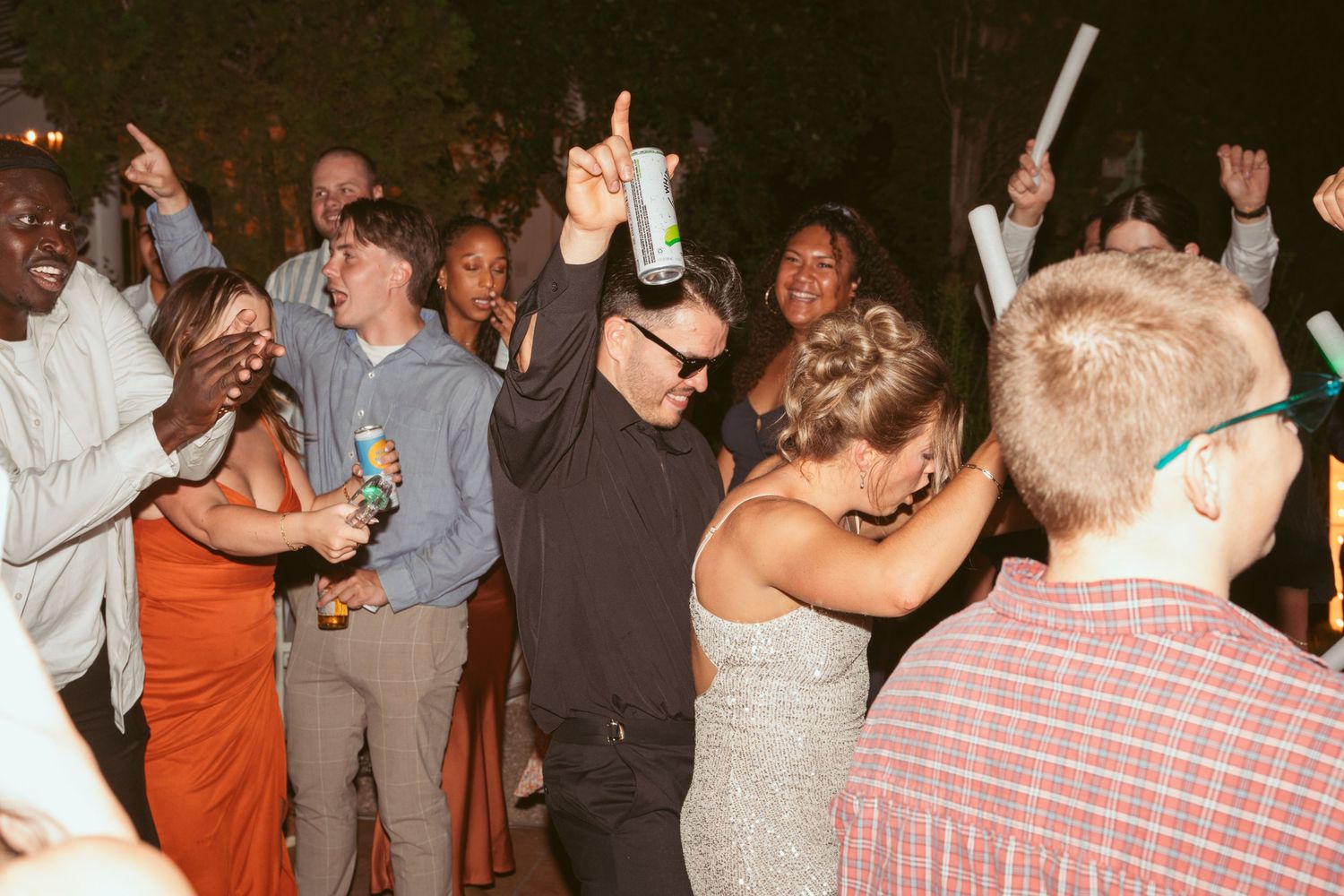 Wedding guests dancing and celebrating with raised arms on a lively dance floor at night.